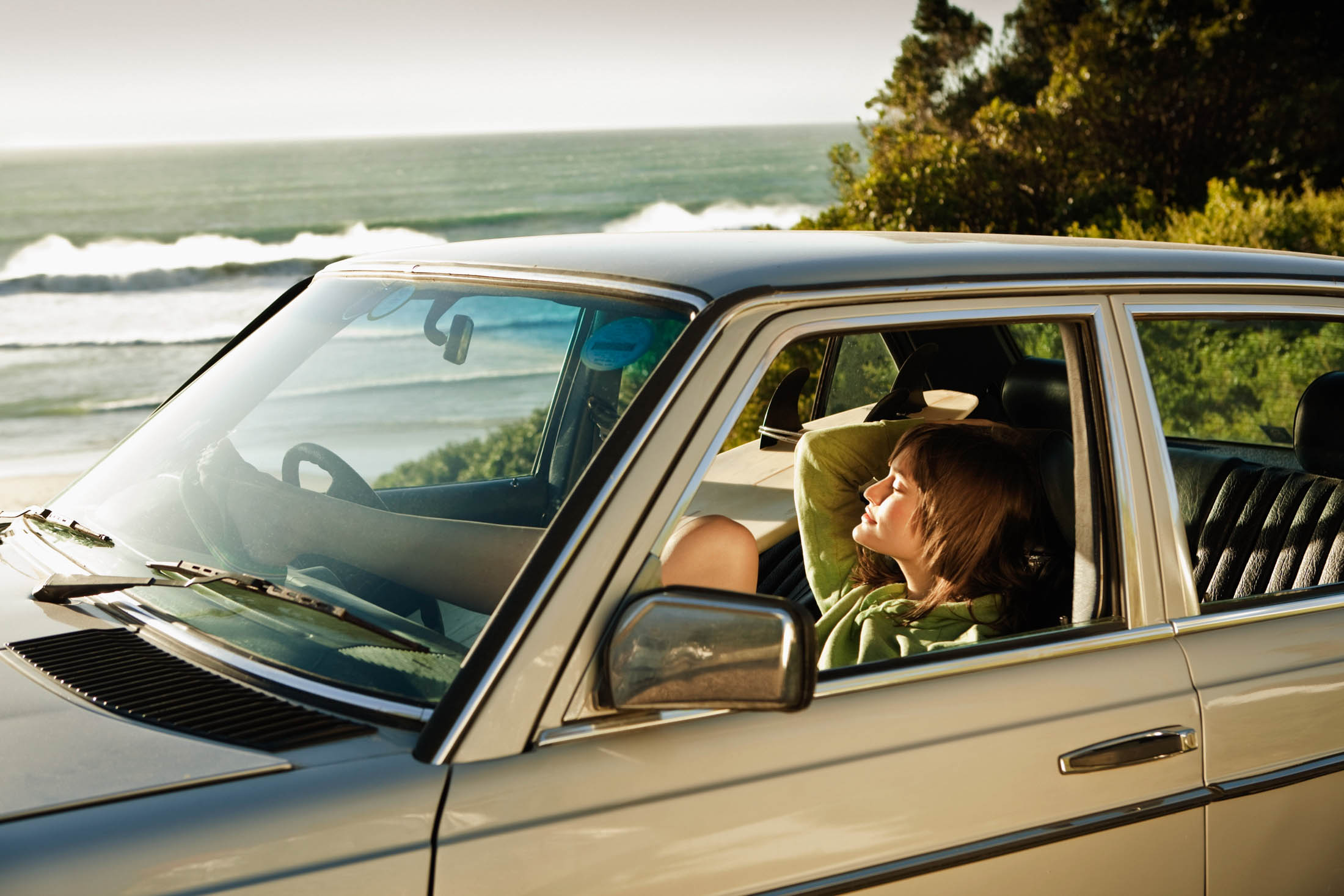 Eine Frau entspannt sich auf dem Beifahrersitz eines am Meer geparkten Oldtimers. Ihre Füße liegen auf dem Armaturenbrett und sie genießt den friedlichen Blick auf das Meer. © Fotografie Tomas Rodriguez