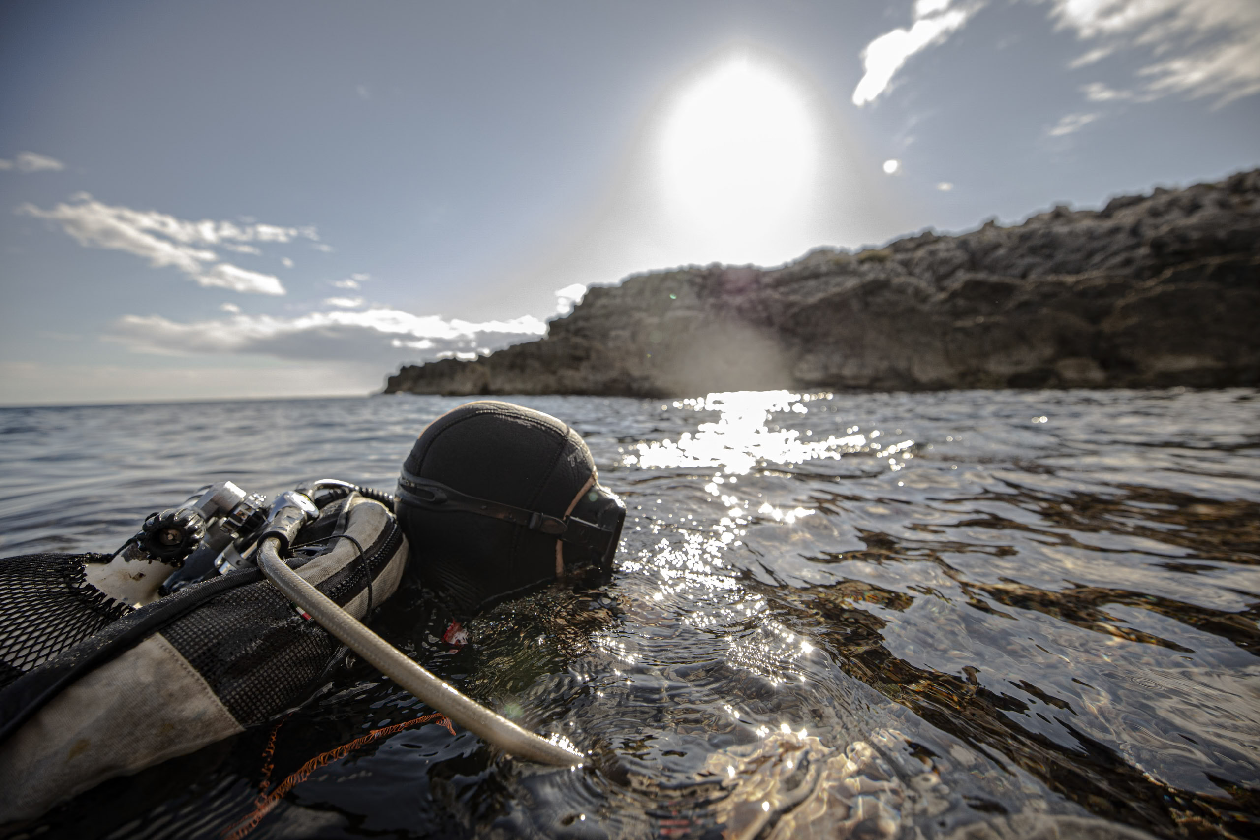 Auf der Meeresoberfläche nahe einer felsigen Küste schwimmt eine Tauchausrüstung, das helle Sonnenlicht spiegelt sich im Wasser. © Fotografie Tomas Rodriguez