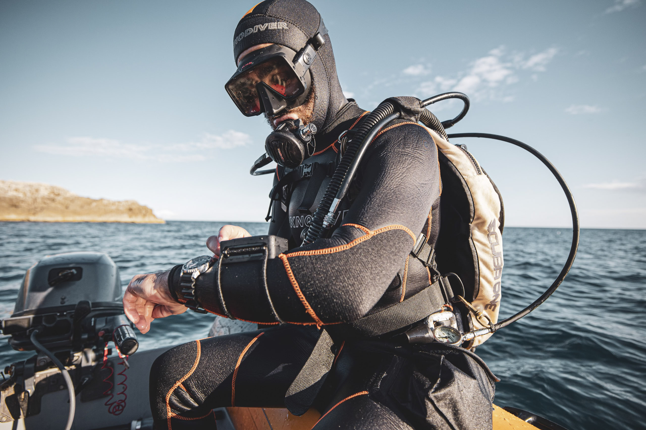 Ein Taucher in voller Montur, mit schwarzem Neoprenanzug und Maske, bereitet seine Ausrüstung auf einem Boot mit Blick auf das klare blaue Wasser vor. © Fotografie Tomas Rodriguez