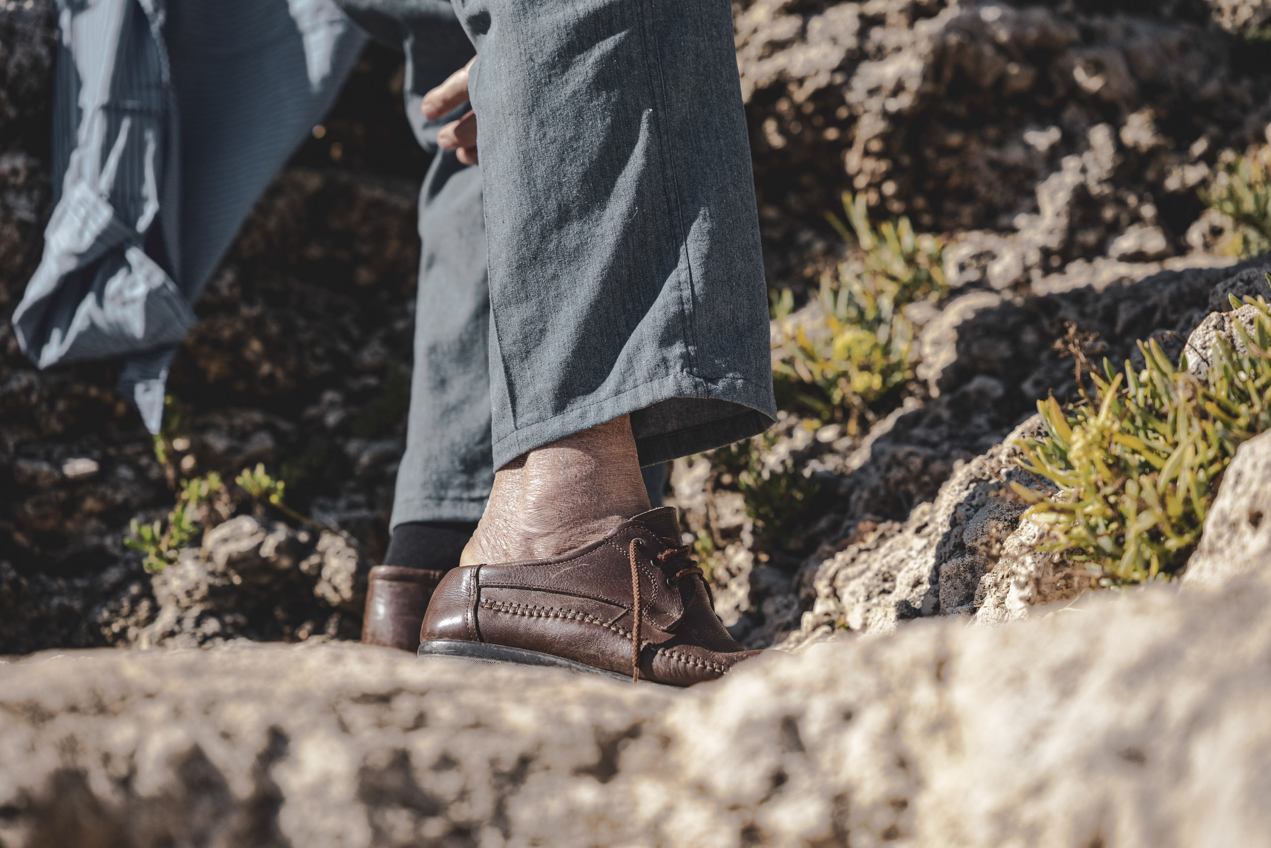 Nahaufnahme der Unterschenkel und Füße einer Person. Sie trägt braune Stiefel und Jeans und steht in felsigem Gelände mit grünen Pflanzen. © Fotografie Tomas Rodriguez