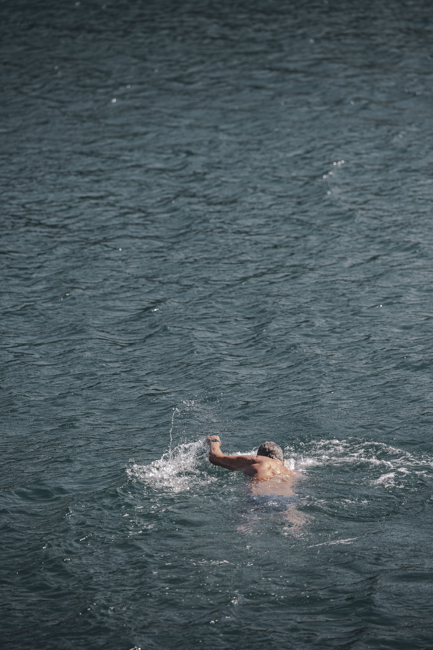 Ein Mann schwimmt in einem Gewässer, von hinten gesehen, mitten im Schwimmzug, wobei sein Arm über der Wasseroberfläche sichtbar ist. © Fotografie Tomas Rodriguez