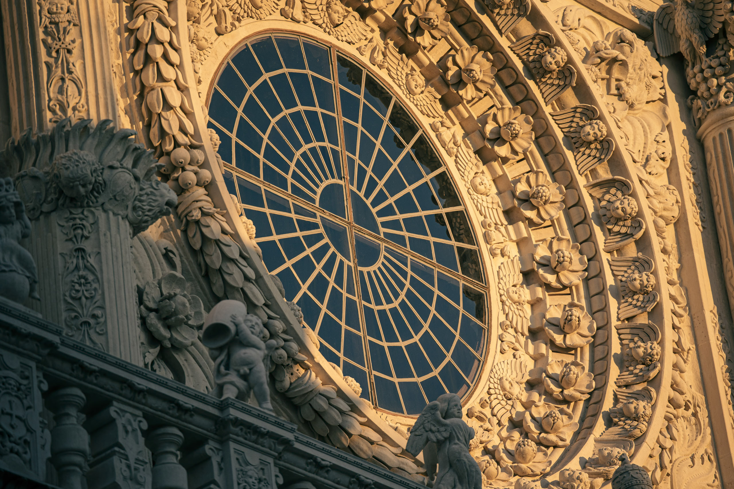 Eine detaillierte Nahaufnahme der reich verzierten Fassade einer Kathedrale mit einem großen, kunstvollen Rosettenfenster mit Buntglas, umgeben von kunstvollen Steinmetzarbeiten und Skulpturen. © Fotografie Tomas Rodriguez