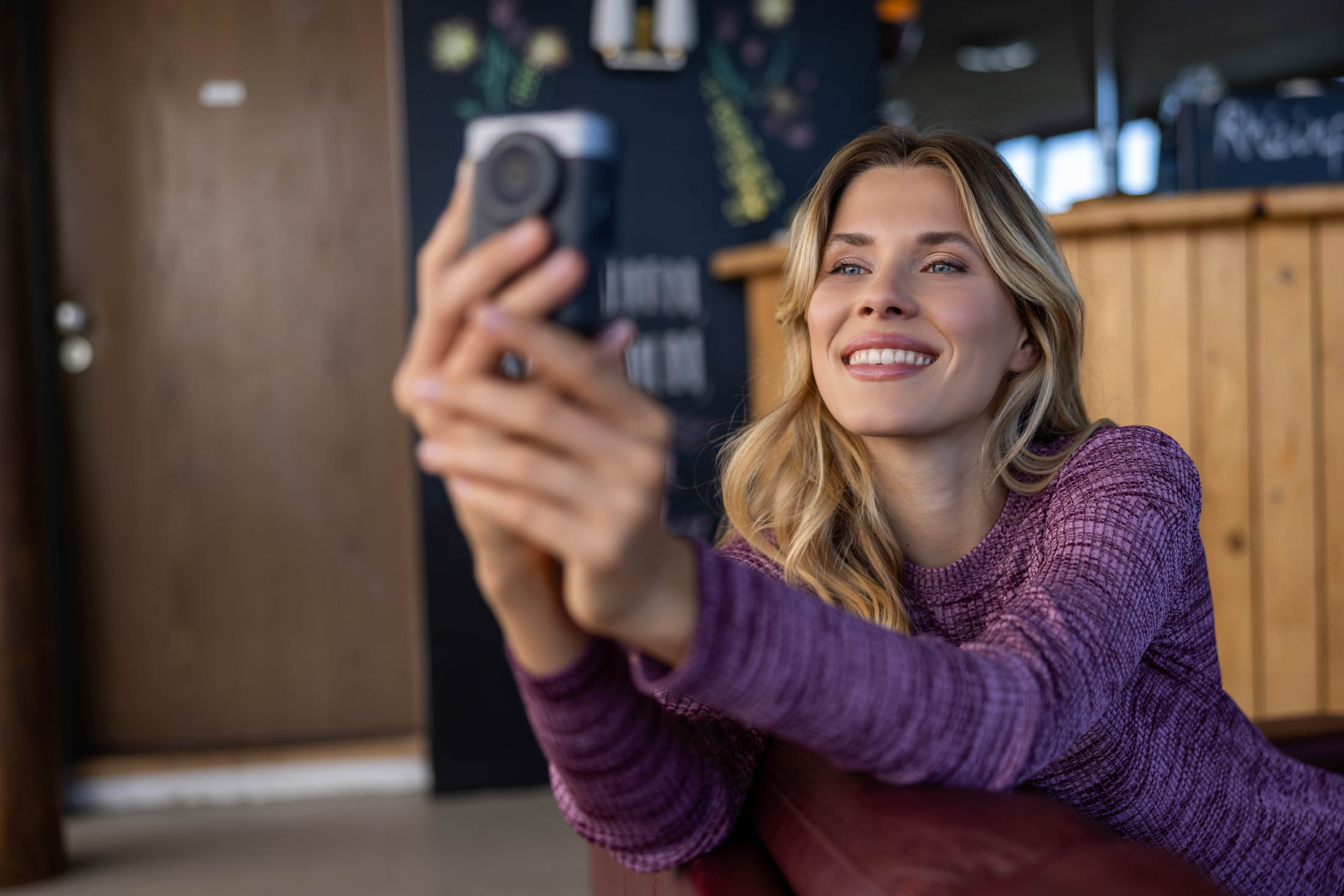 Eine lächelnde Frau im lila Pullover macht in einem gemütlichen, holzgetäfelten Raum ein Selfie mit ihrem Smartphone. © Fotografie Tomas Rodriguez