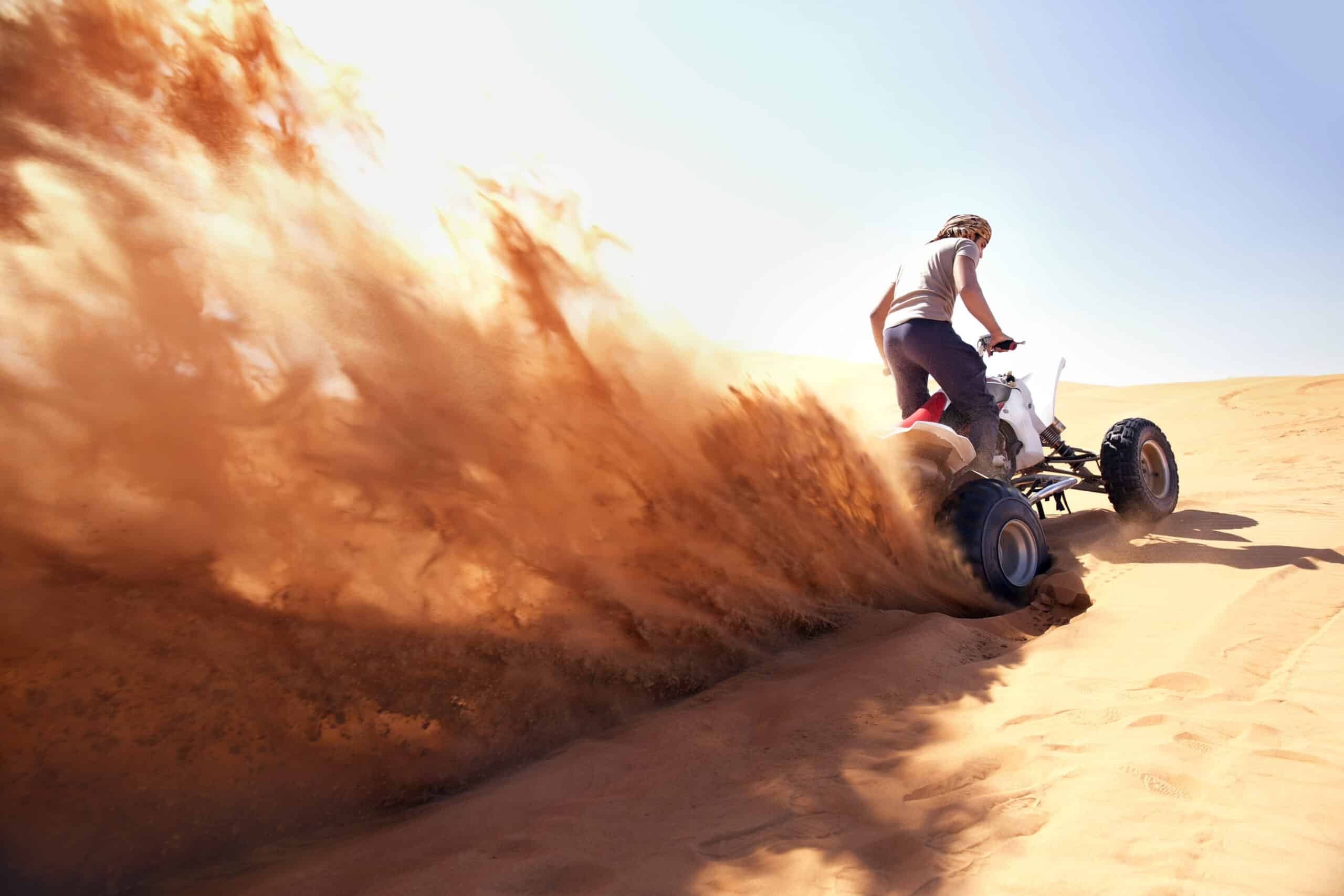 Eine Person auf einem Geländefahrzeug wirbelt eine große Sandwolke auf, während sie unter klarem Himmel über eine Düne in einer Wüste rast. © Fotografie Tomas Rodriguez