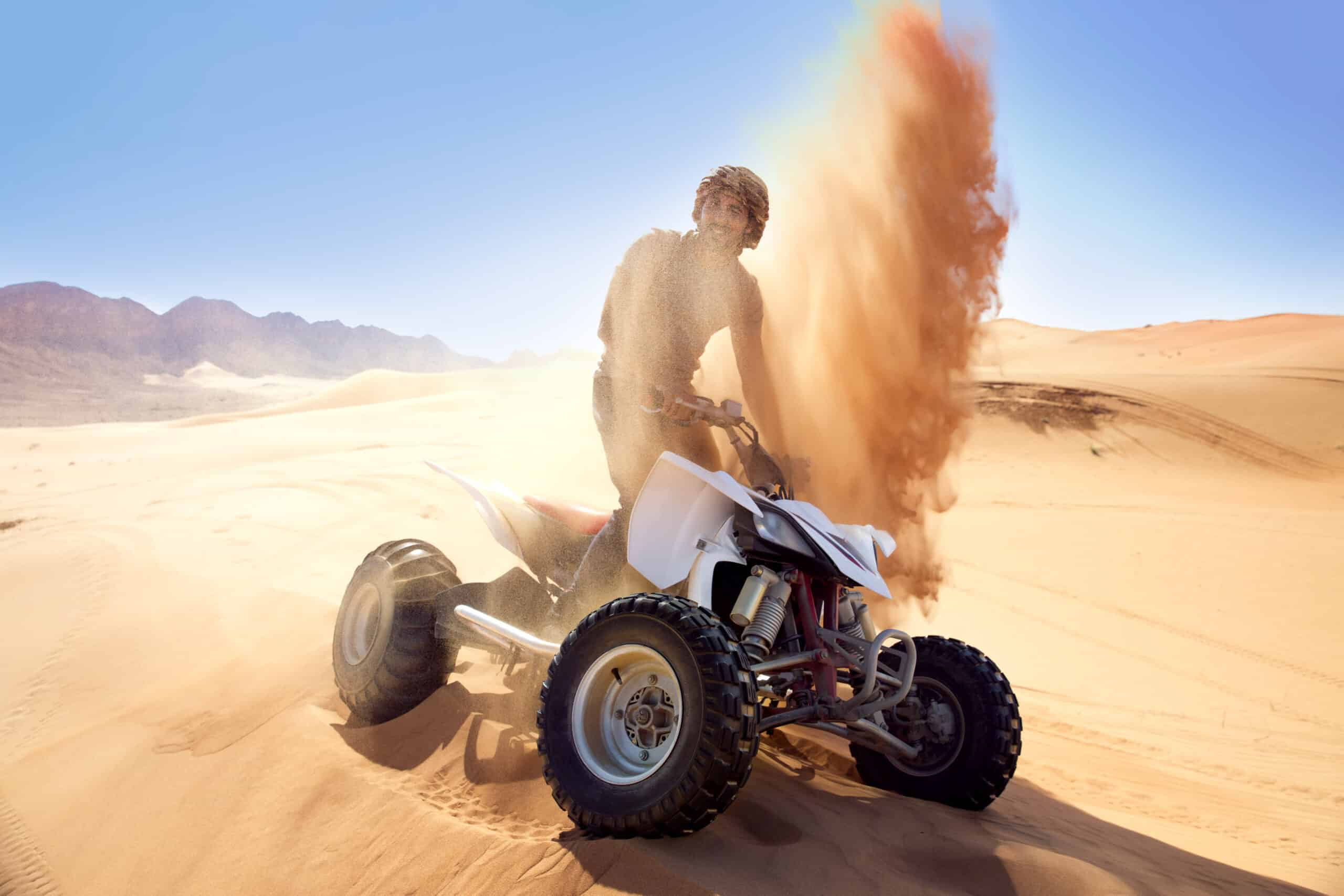 Eine Person fährt auf einem weißen Geländefahrzeug durch die Wüste und wirbelt unter einem klaren blauen Himmel eine Sandspur hinter sich auf. © Fotografie Tomas Rodriguez