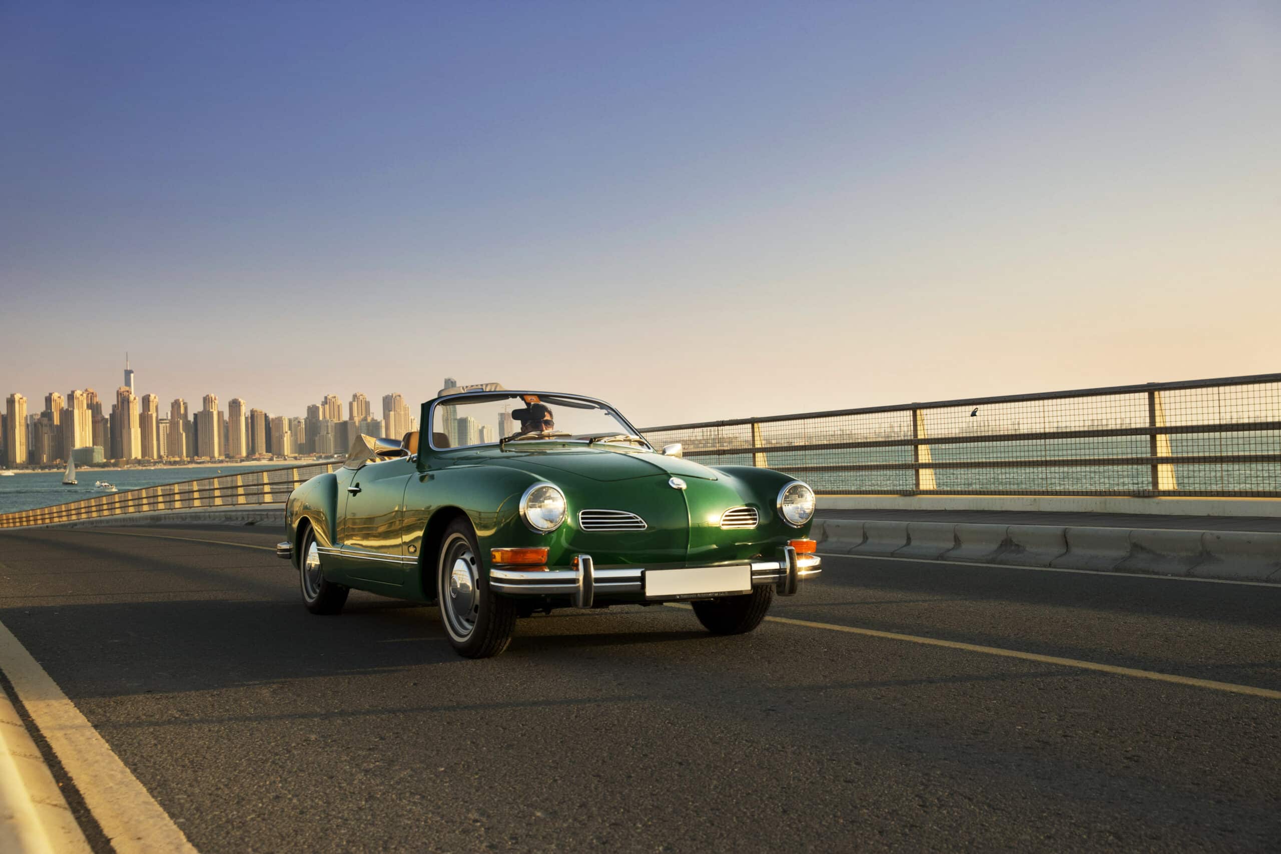 Ein grünes Oldtimer-Cabrio fährt auf einer Küstenstraße mit der Skyline einer Stadt im Hintergrund unter einem klaren Himmel. © Fotografie Tomas Rodriguez