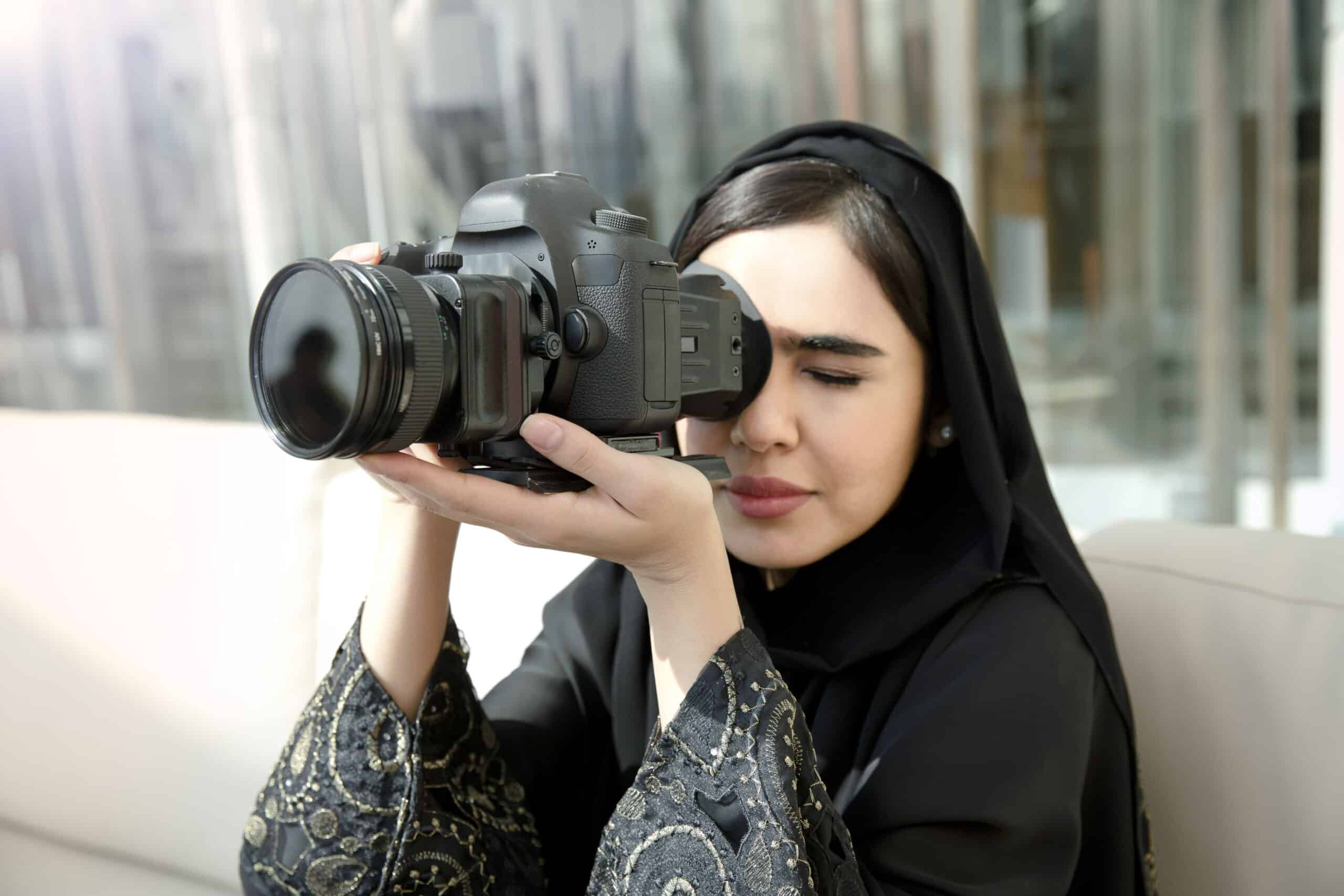 Eine Frau mit Hijab hält konzentriert eine professionelle Kamera in der Hand und bereitet sich darauf vor, in einem Innenbereich ein Foto zu machen. © Fotografie Tomas Rodriguez