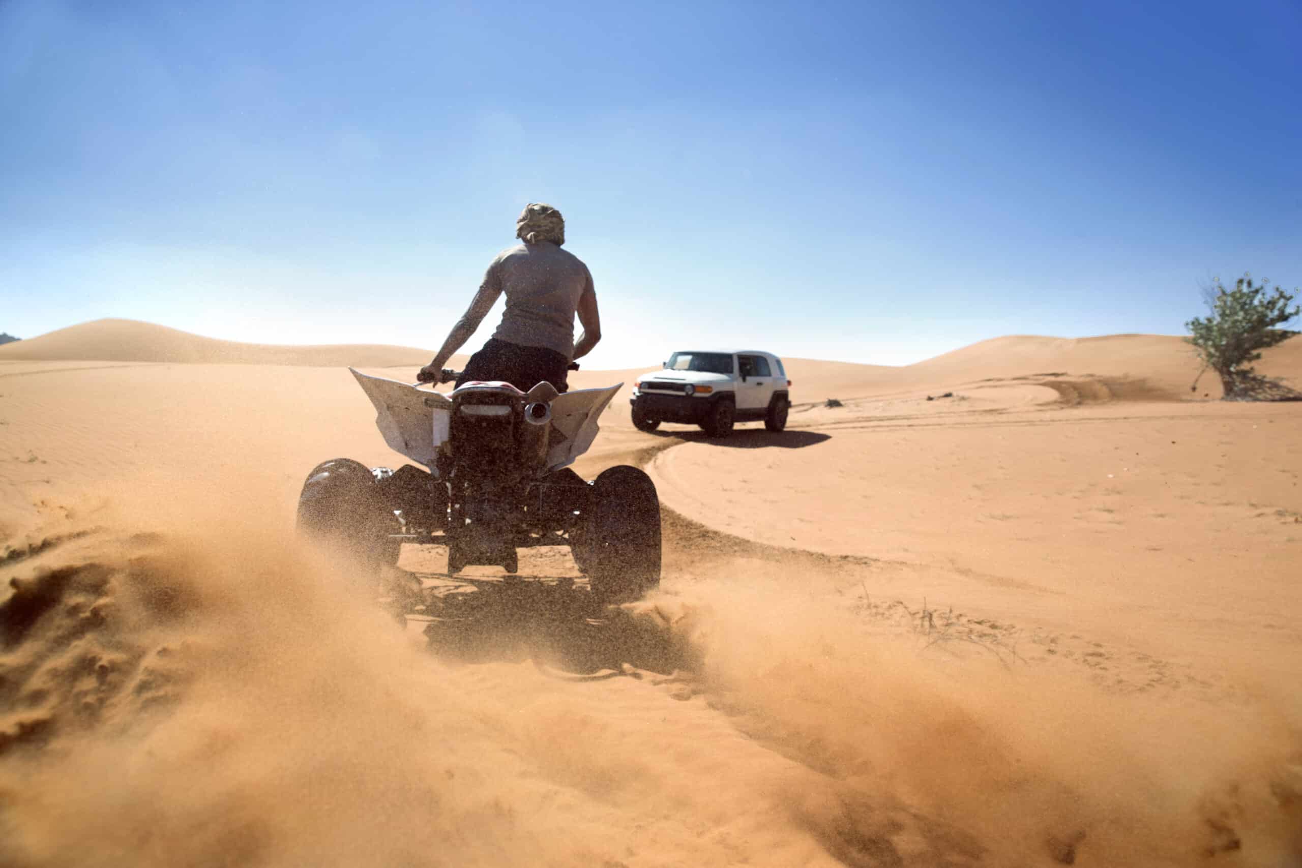 Eine Person fährt mit einem Geländefahrzeug durch die Wüste und wirbelt Sand auf. Im Hintergrund sind unter einem klaren Himmel zwei Allradfahrzeuge zu sehen. © Fotografie Tomas Rodriguez
