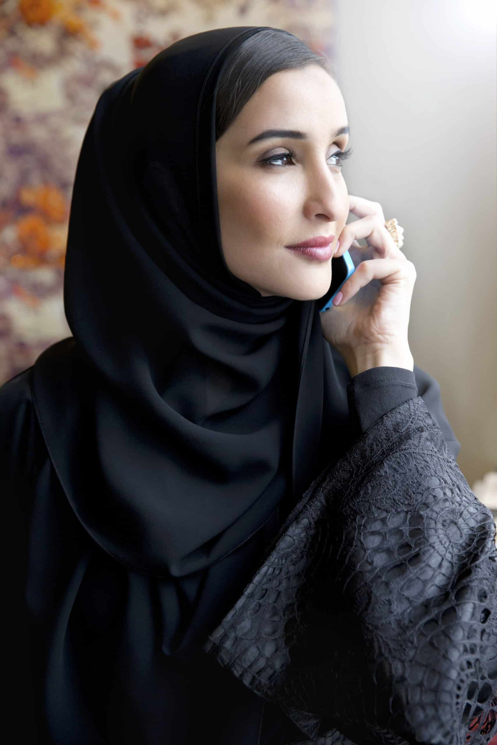 Eine Frau mit Hijab spricht in ein Smartphone und blickt nachdenklich aus dem Fenster. Der Fokus liegt auf ihrem gelassenen Gesichtsausdruck und den eleganten Details ihrer Kleidung. © Fotografie Tomas Rodriguez