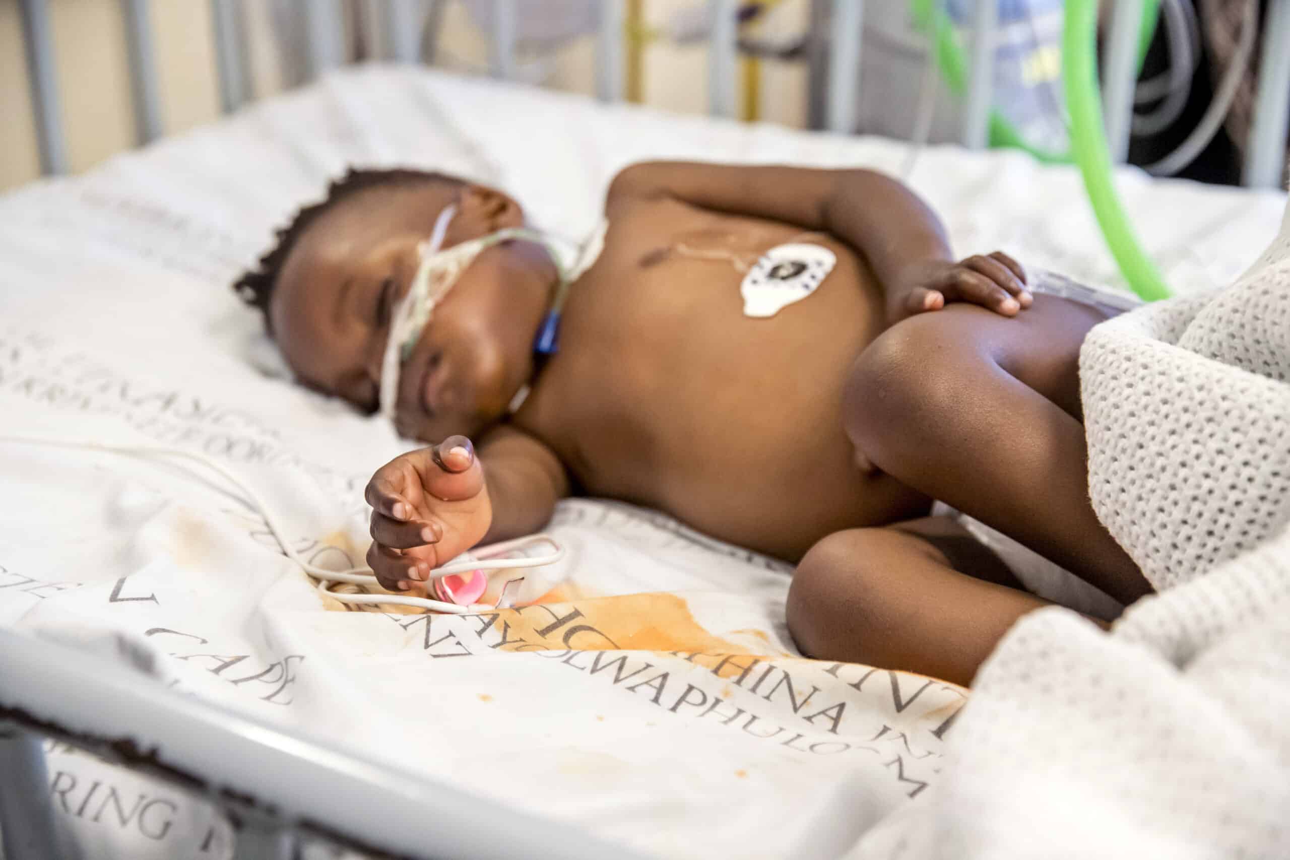 Ein Neugeborenes mit dunkler Haut ruht friedlich in einem Krankenhausbett. Es trägt eine Windel und ist an medizinische Überwachungsgeräte angeschlossen. © Fotografie Tomas Rodriguez