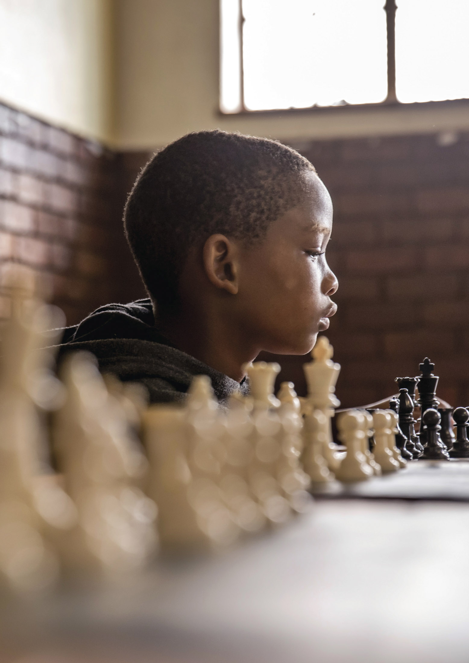 Ein kleiner Junge spielt Schach und ist in Gedanken versunken. Er konzentriert sich in einem warm beleuchteten Raum intensiv auf das Schachbrett. © Fotografie Tomas Rodriguez