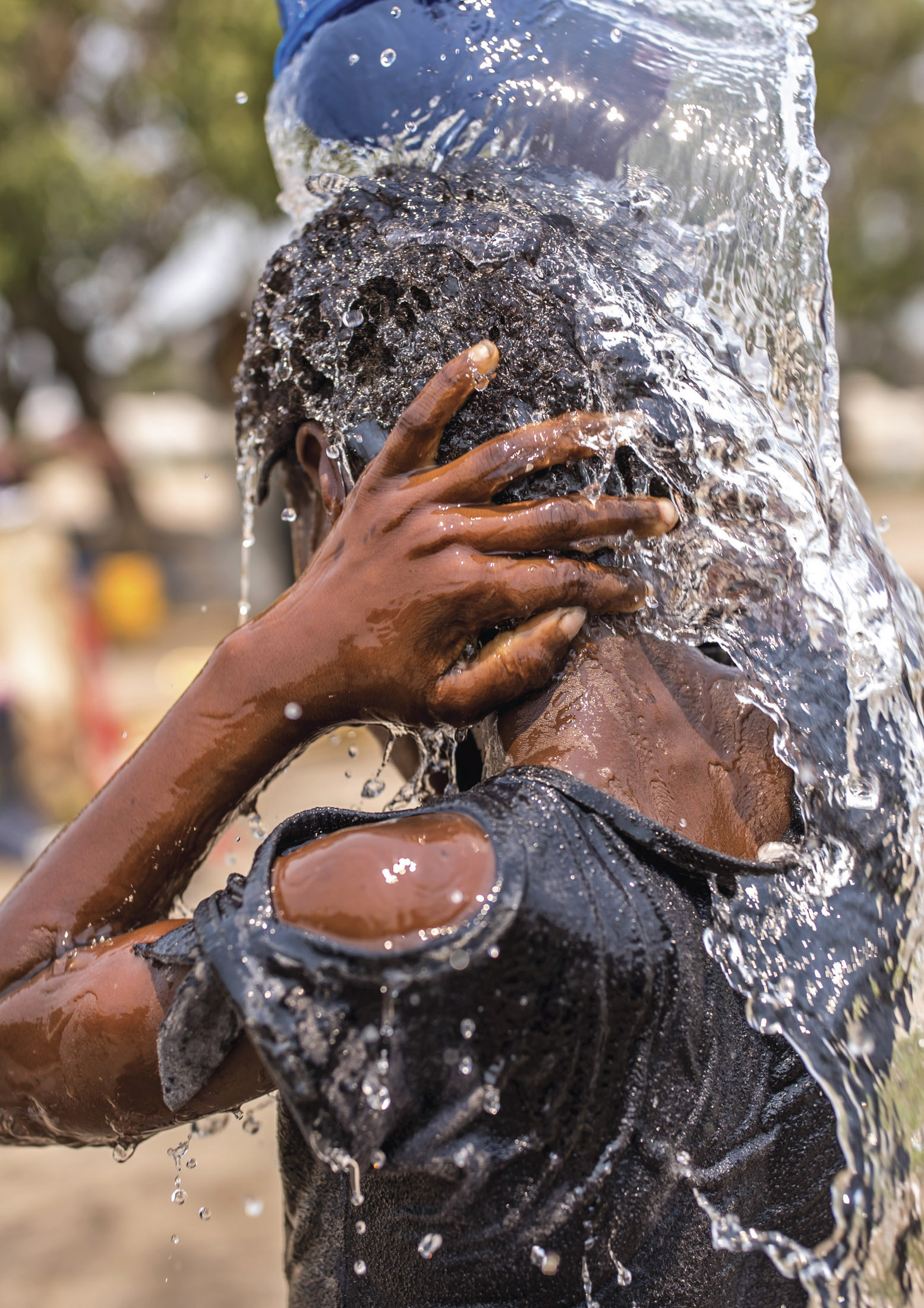 Eine Person ist durchnässt und bedeckt ihr Gesicht mit den Händen, während ein großer Spritzer ihren Kopf und ihre Schultern umhüllt. Tropfen und Bewegung des Wassers im Detail vor einem unscharfen Hintergrund aufgenommen. © Fotografie Tomas Rodriguez