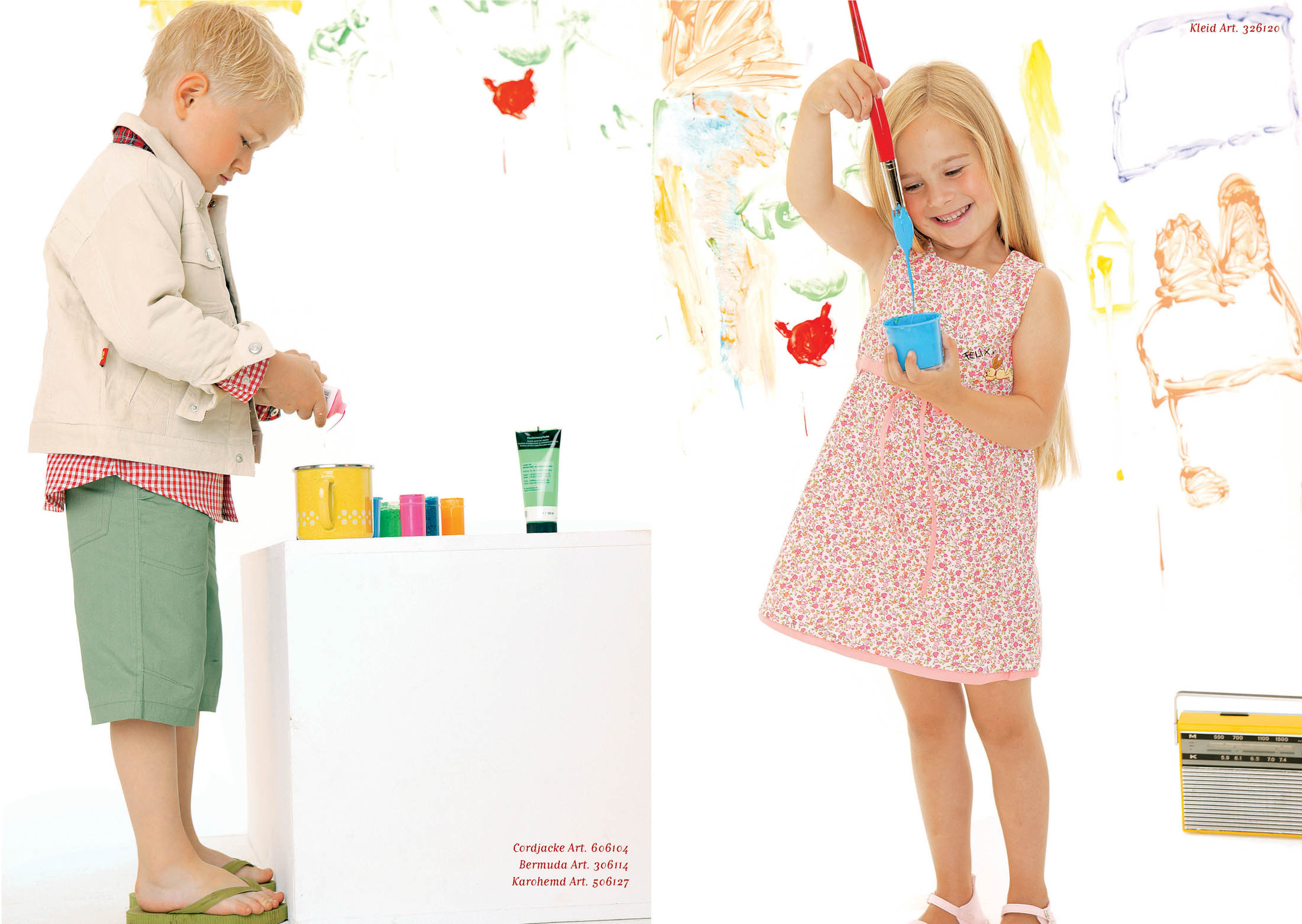 Zwei kleine Kinder malen fröhlich auf einer weißen Leinwand, umgeben von Malutensilien und bunten Handabdrücken an der Wand. Ein Junge gießt Farbe in den Topf und ein Mädchen benutzt einen Pinsel. © Fotografie Tomas Rodriguez
