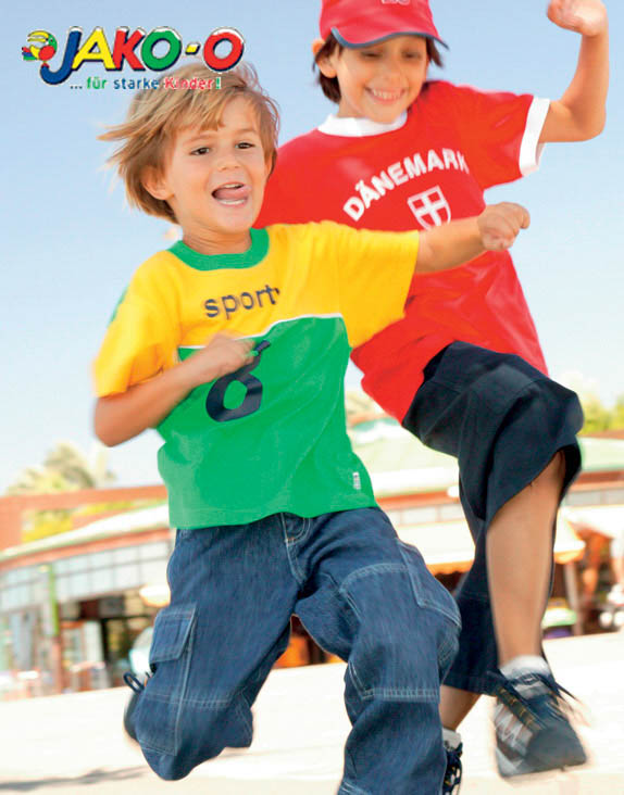 Zwei fröhliche Kinder spielen Fangen, eines in einem grün-gelben T-Shirt und das andere in einem roten T-Shirt mit der Aufschrift „Dänemark“. Beide lächeln und rennen voller Energie. © Fotografie Tomas Rodriguez