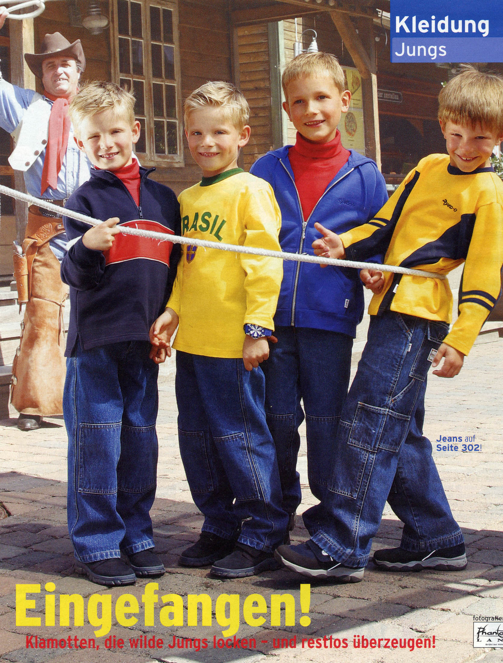 Vier junge Jungen spielen Tauziehen auf einer gepflasterten Straße, im Hintergrund achtet ein Erwachsener auf sie. Sie tragen farbenfrohe, legere Kleidung und wirken fröhlich. Der Text „Eingefangen! Kleidung Jungs“ fällt auf. © Fotografie Tomas Rodriguez