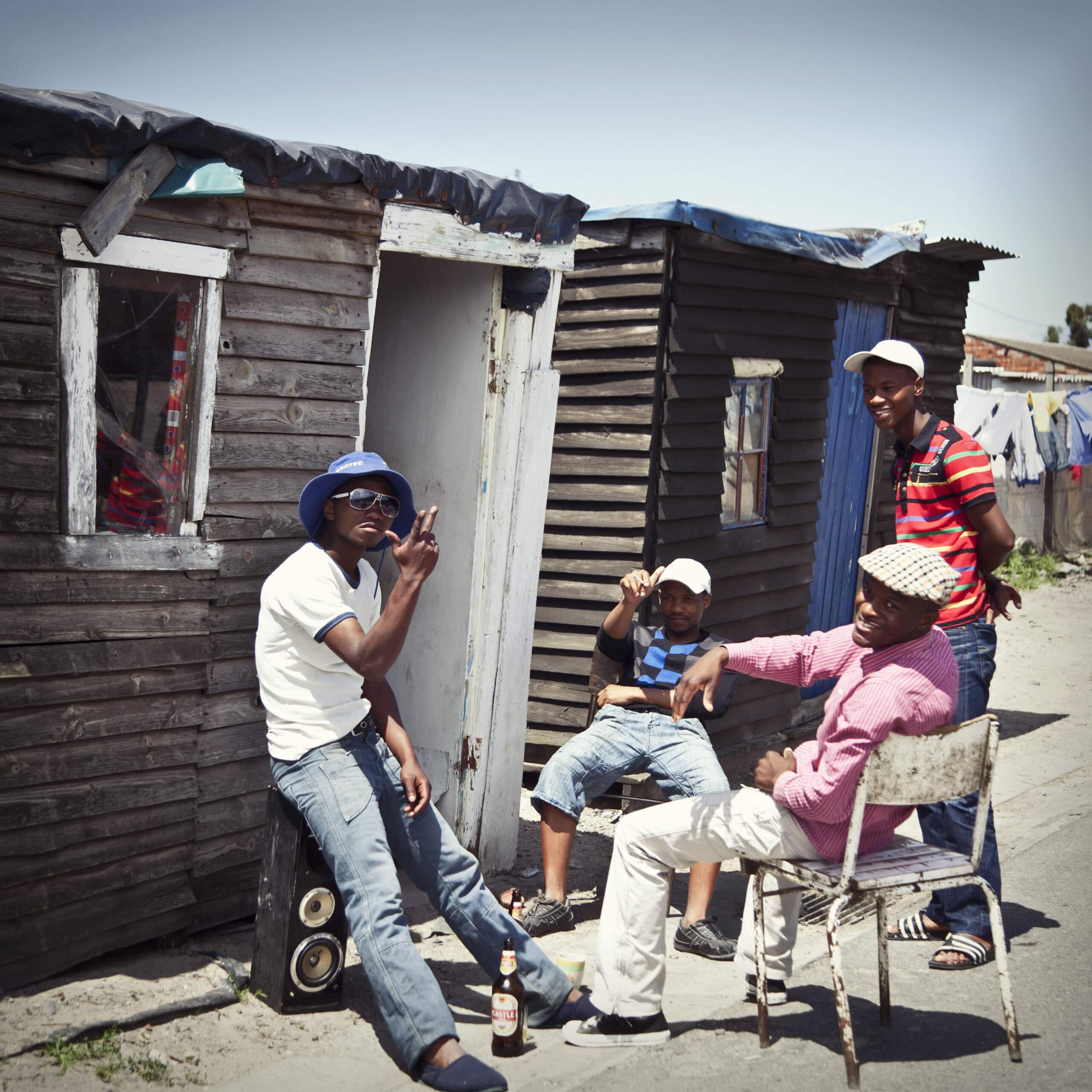 Vier Männer unterhalten sich ungezwungen vor einer provisorischen Holzhütte in sonniger Umgebung. Zwei sitzen auf Stühlen, einer lehnt an der Hütte und der vierte steht und unterhält sich mit der Gruppe. © Fotografie Tomas Rodriguez