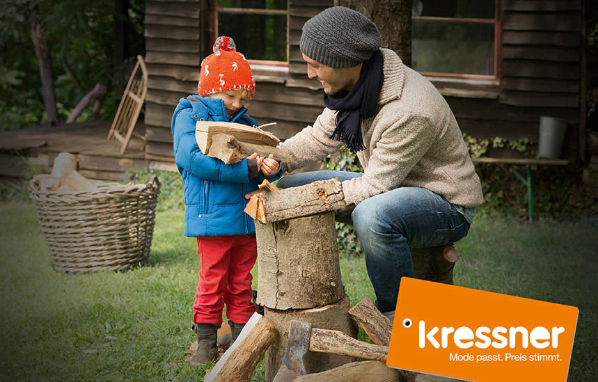 Ein Mann und ein Kind in Jacken und Hüten sind im Freien. Das Kind hält eine kleine Handsäge und schneidet unter Anleitung des Mannes Holz auf einem Baumstumpf. Im Hintergrund sind ein Korb und Stühle zu sehen. © Fotografie Tomas Rodriguez