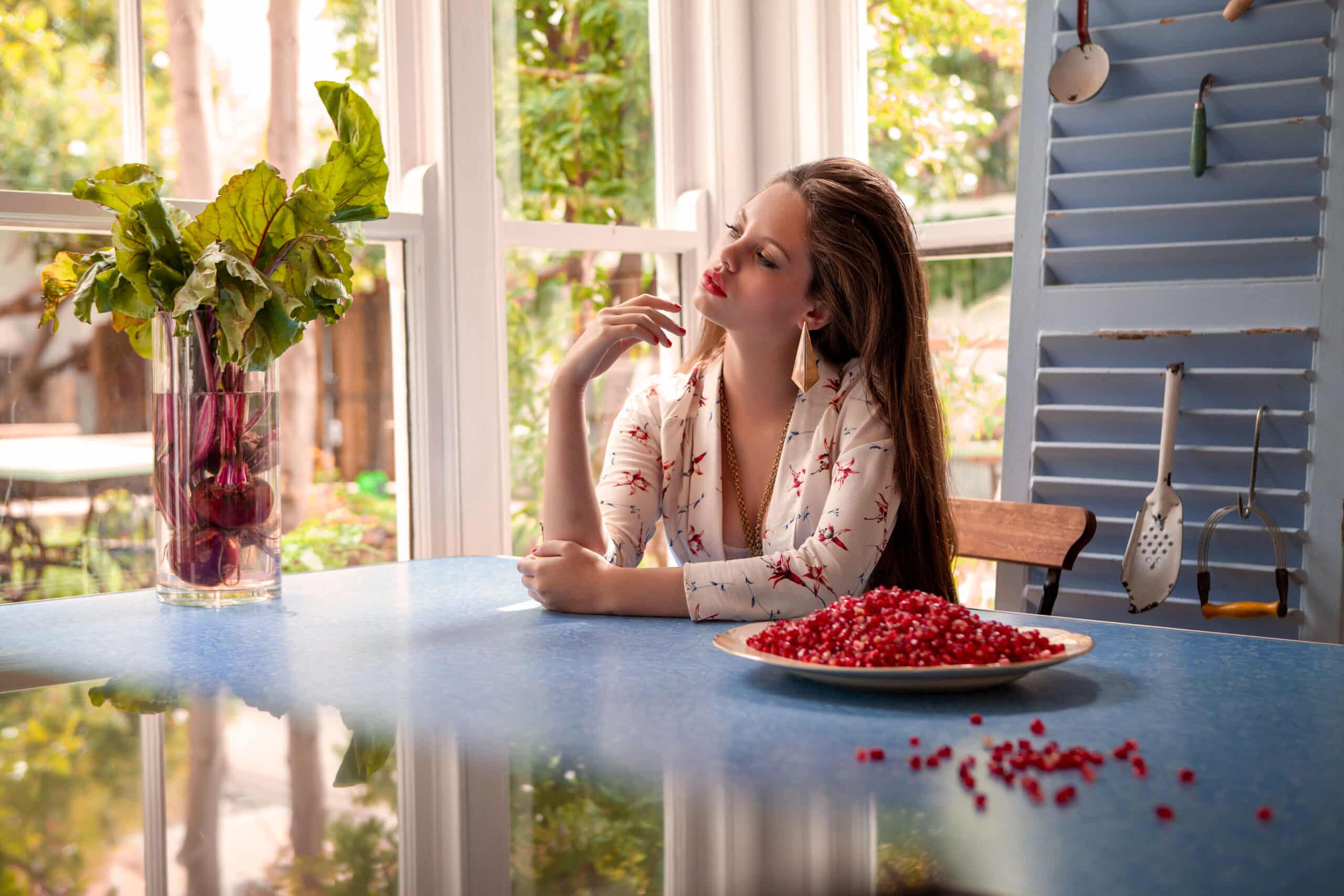 Eine Frau sitzt nachdenklich an einem Küchentisch am Fenster. Vor ihr steht ein Teller mit roten Johannisbeeren, auf dem Tisch sind verstreut Beeren verstreut, in einem gemütlichen, sonnendurchfluteten Raum. © Fotografie Tomas Rodriguez