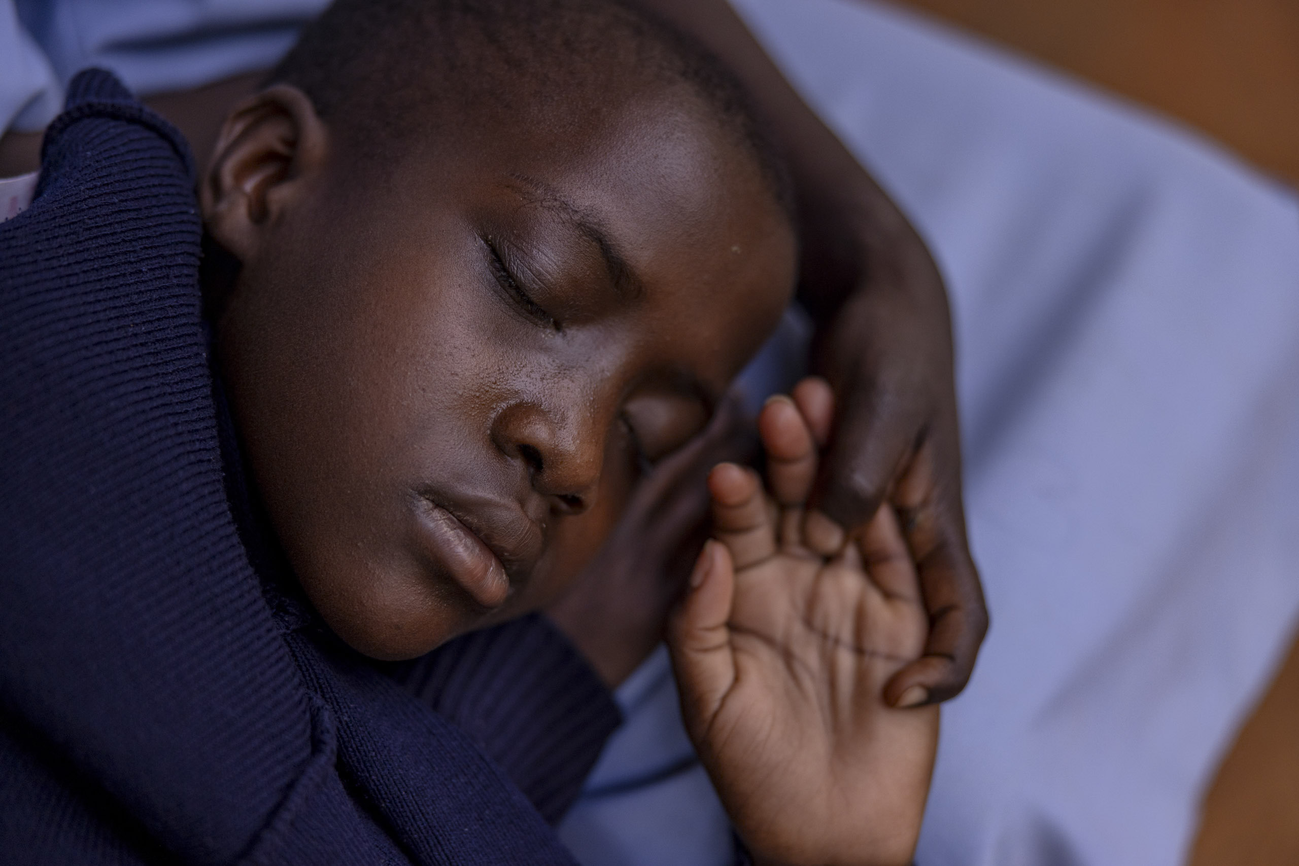 Ein kleiner Junge schläft friedlich auf einer hellen Decke und trägt einen dunklen Pullover. Sein Kopf ruht sanft auf seinen Armen und zeigt einen heiteren Gesichtsausdruck. © Fotografie Tomas Rodriguez
