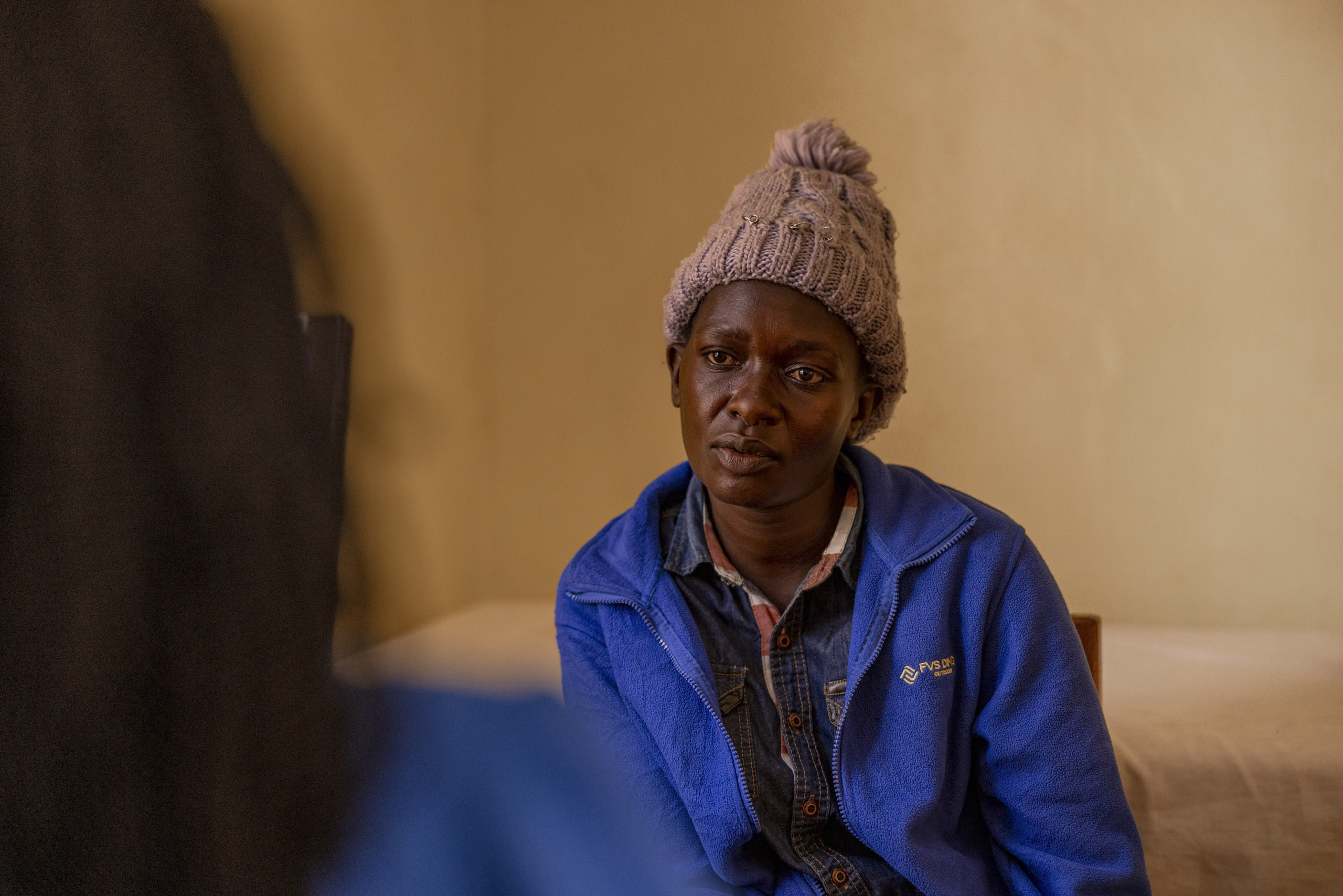 Eine konzentrierte Frau mit Strickmütze und blauer Jacke hört in einem Innenbereich aufmerksam zu, während im Vordergrund eine weitere Person zu sehen ist. © Fotografie Tomas Rodriguez