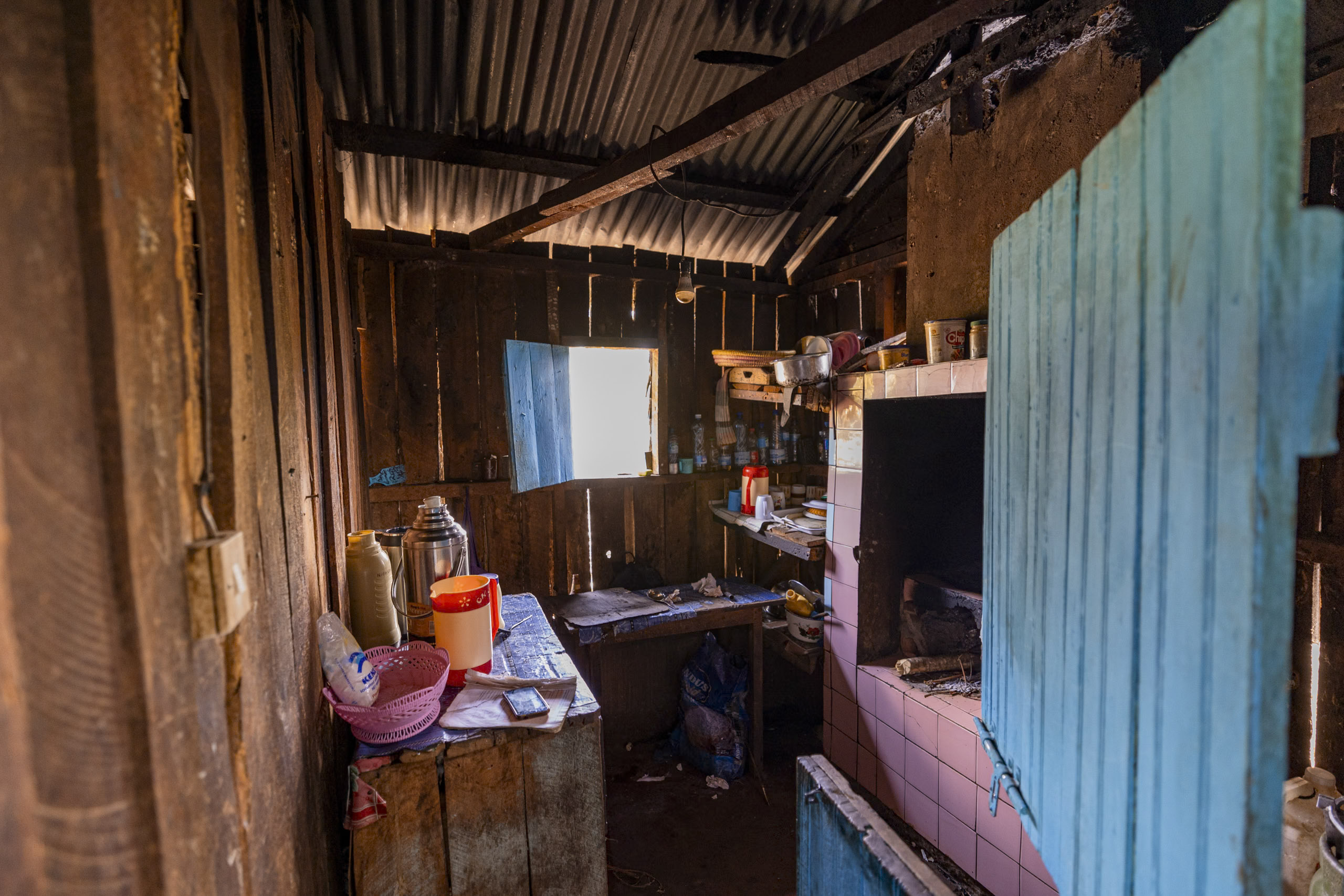 Innenansicht einer heruntergekommenen Küche mit rostigen Metallwänden, einer überfüllten Arbeitsplatte und einem alten Herd. Sonnenlicht fällt durch ein Fenster und hebt den abgenutzten Zustand hervor. © Fotografie Tomas Rodriguez
