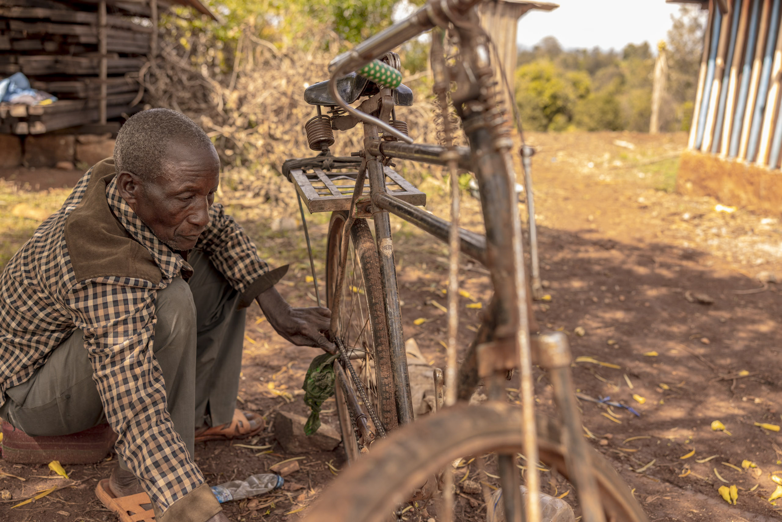 Ein älterer Mann repariert in ländlicher Umgebung ein Fahrrad. Er arbeitet konzentriert an dem Rad, das er aufrecht und mit einem Stock gestützt abstellt. © Fotografie Tomas Rodriguez