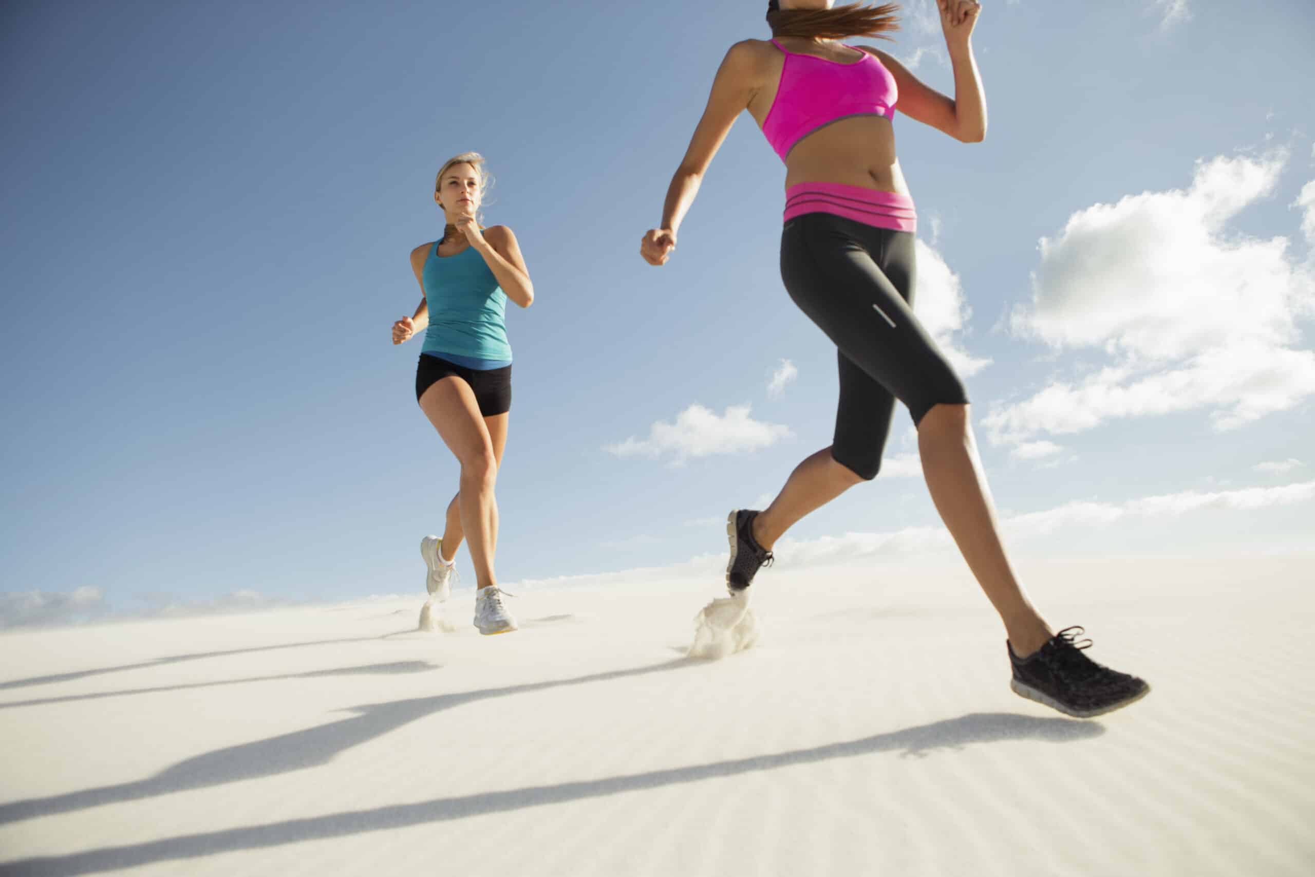 Zwei Frauen, die an einem sonnigen Tag in Sportkleidung an einem Sandstrand laufen. Der Fokus liegt auf ihrer Bewegung und der sie umgebenden Natur. © Fotografie Tomas Rodriguez