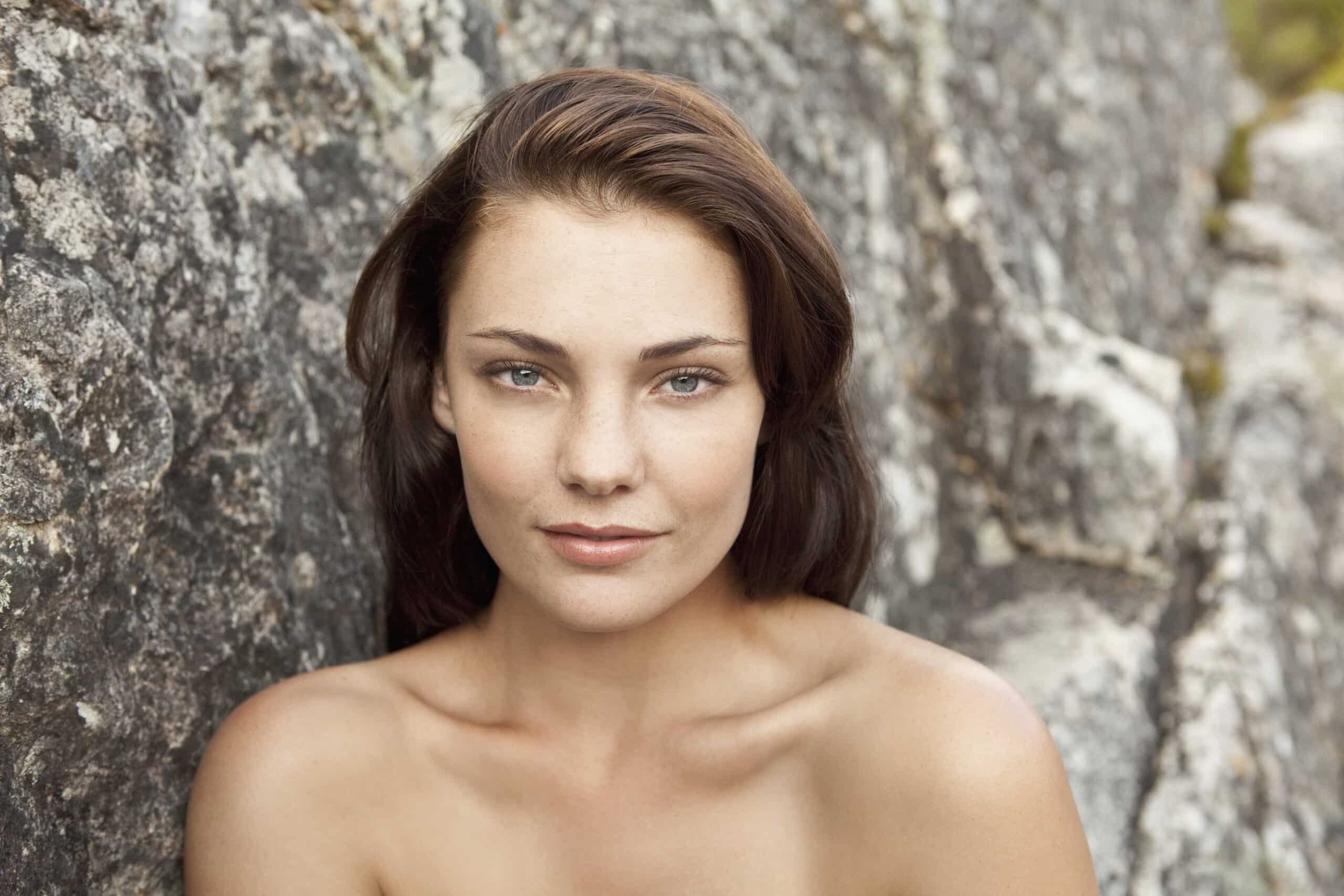 Eine Frau mit dunklem Haar und dezentem Make-up sitzt vor einer schroffen Steinmauer und blickt mit sanftem Gesichtsausdruck direkt in die Kamera. © Fotografie Tomas Rodriguez