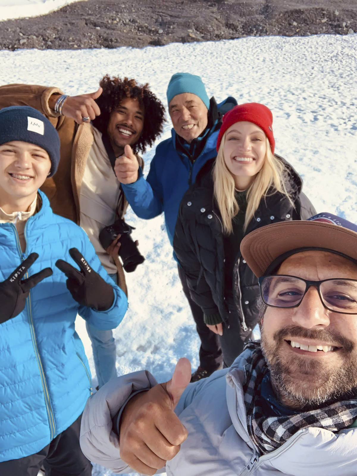 Eine Gruppe von fünf Personen in Winterkleidung, die lächelnd in einer verschneiten Landschaft für ein Selfie posieren. Zwei Personen zeigen den Daumen nach oben, eine Person zeigt das Peace-Zeichen und alle wirken fröhlich. Im Hintergrund sind Schnee und felsiges Gelände zu sehen. © Fotografie Tomas Rodriguez