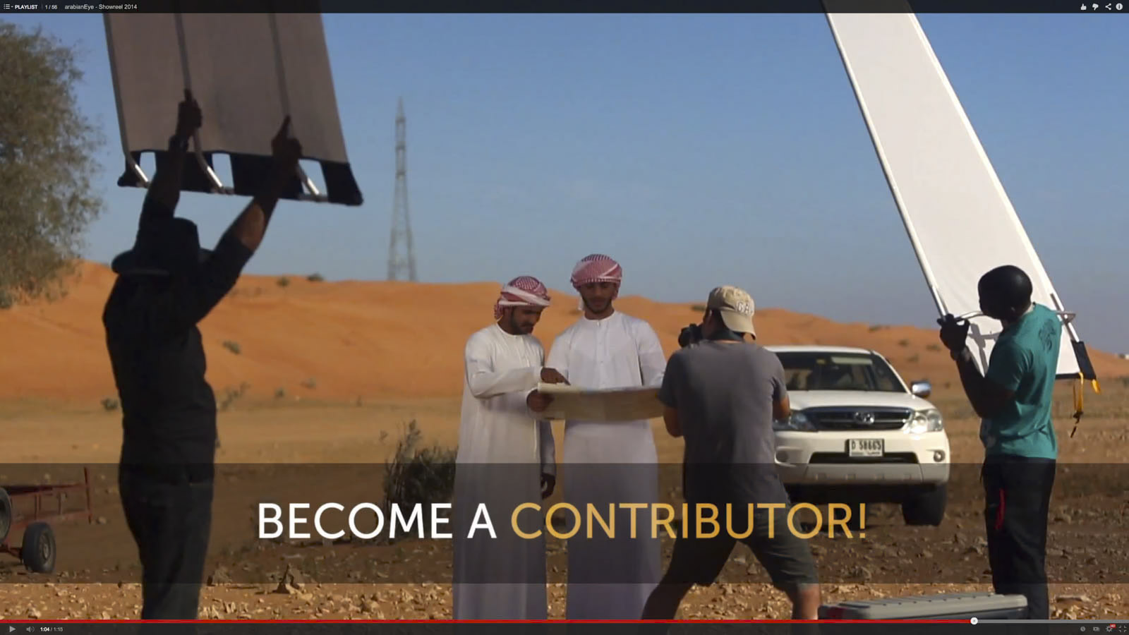 Ein Filmteam dreht eine Szene in einer Wüstenlandschaft. Zwei Männer in traditioneller orientalischer Kleidung untersuchen eine Karte. Die Crewmitglieder benutzen Beleuchtungsgeräte. In der Nähe parkt ein weißer SUV. Text unten: „WERDEN SIE MITARBEITER!“ © Fotografie Tomas Rodriguez