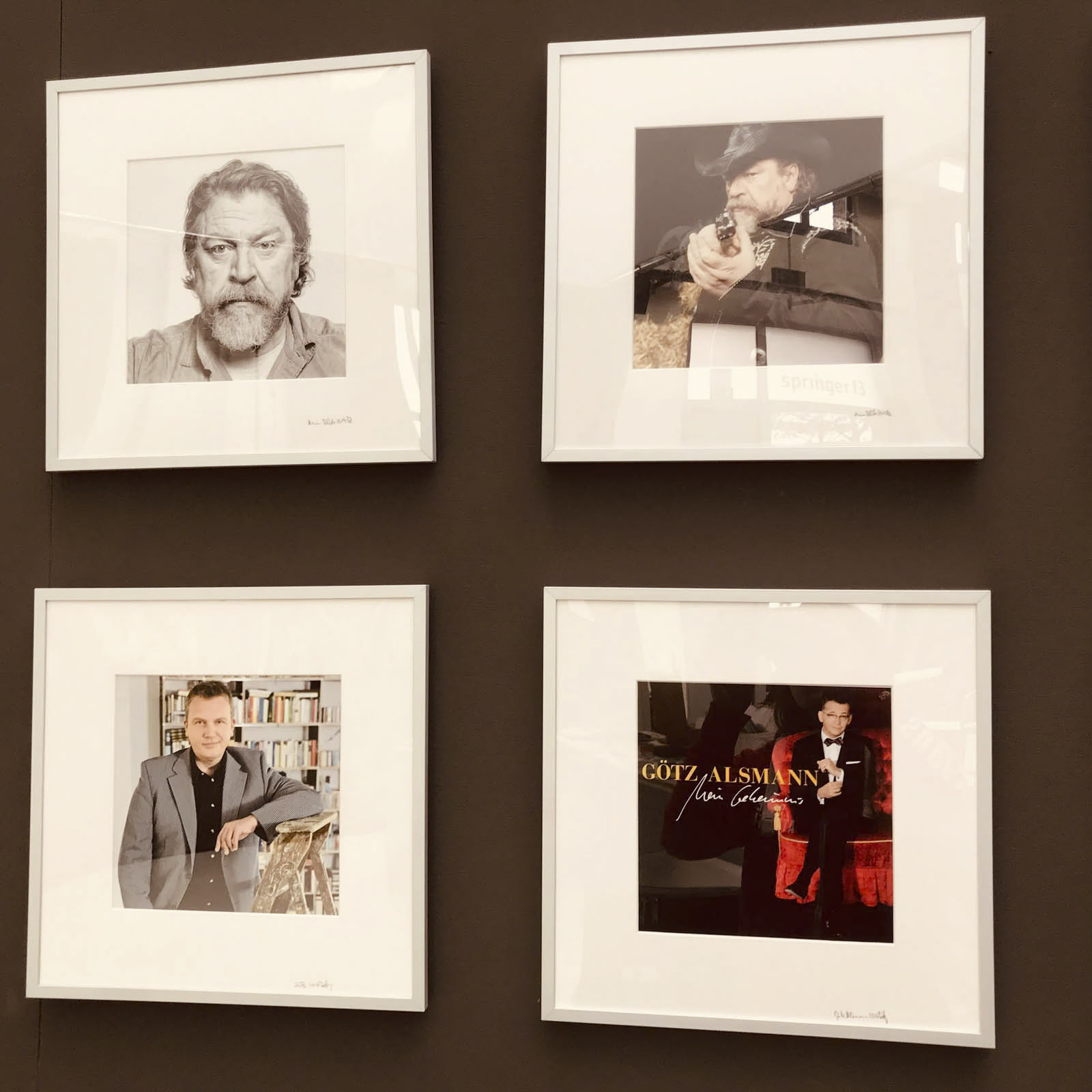 An einer Wand hängen vier gerahmte Bilder. Das Bild oben links ist ein Schwarzweißporträt eines Mannes mit Bart. Das Bild oben rechts zeigt ein Schwarzweißbild einer Person, die mit einer Waffe zielt. Das Bild unten links zeigt einen Mann im Anzug. Unten rechts ist ein Albumcover zu sehen. © Fotografie Tomas Rodriguez