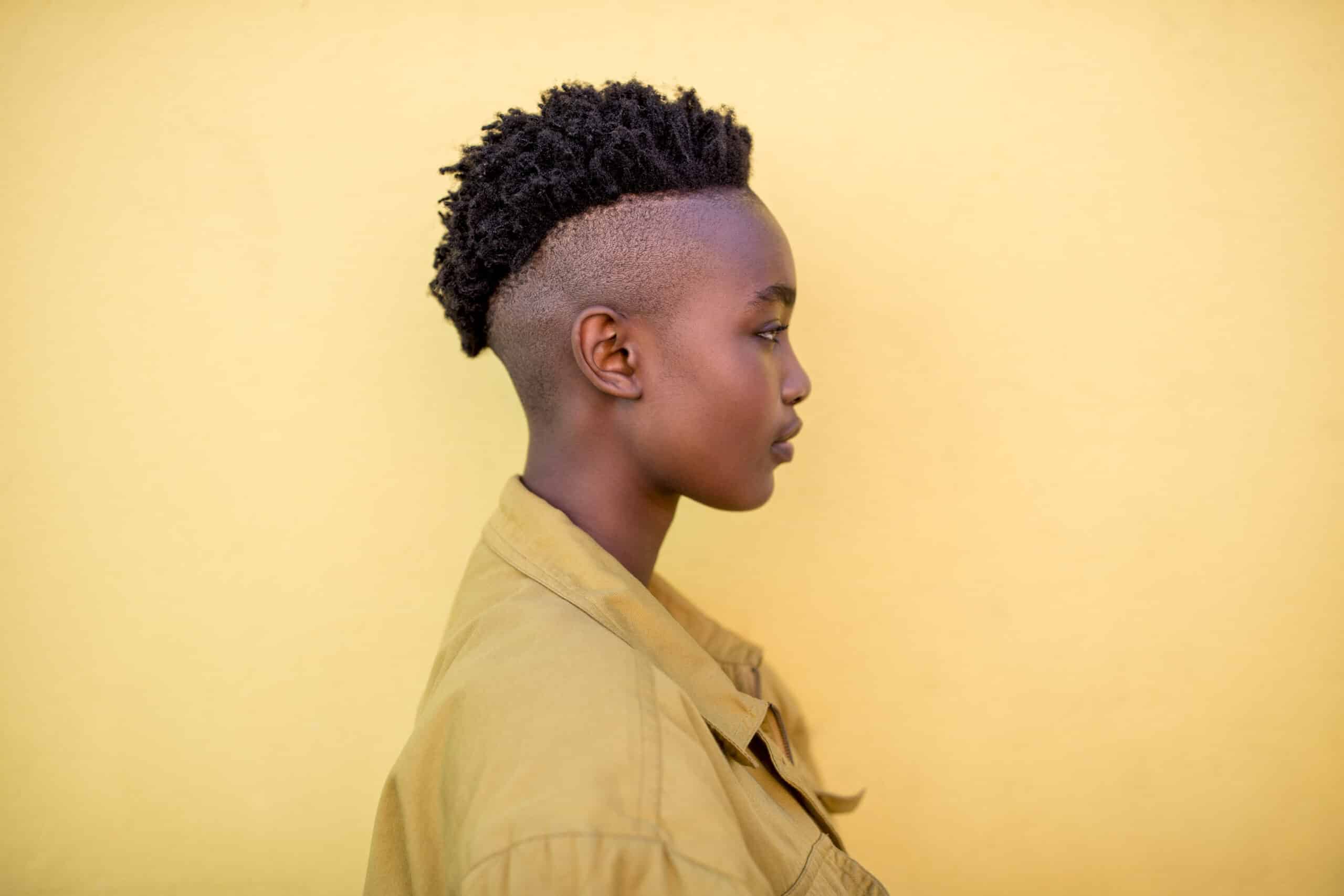 Seitenprofil einer jungen Person mit stylischem, modernem Haarschnitt, die ein beiges Hemd vor einem schlichten gelben Hintergrund trägt. © Fotografie Tomas Rodriguez