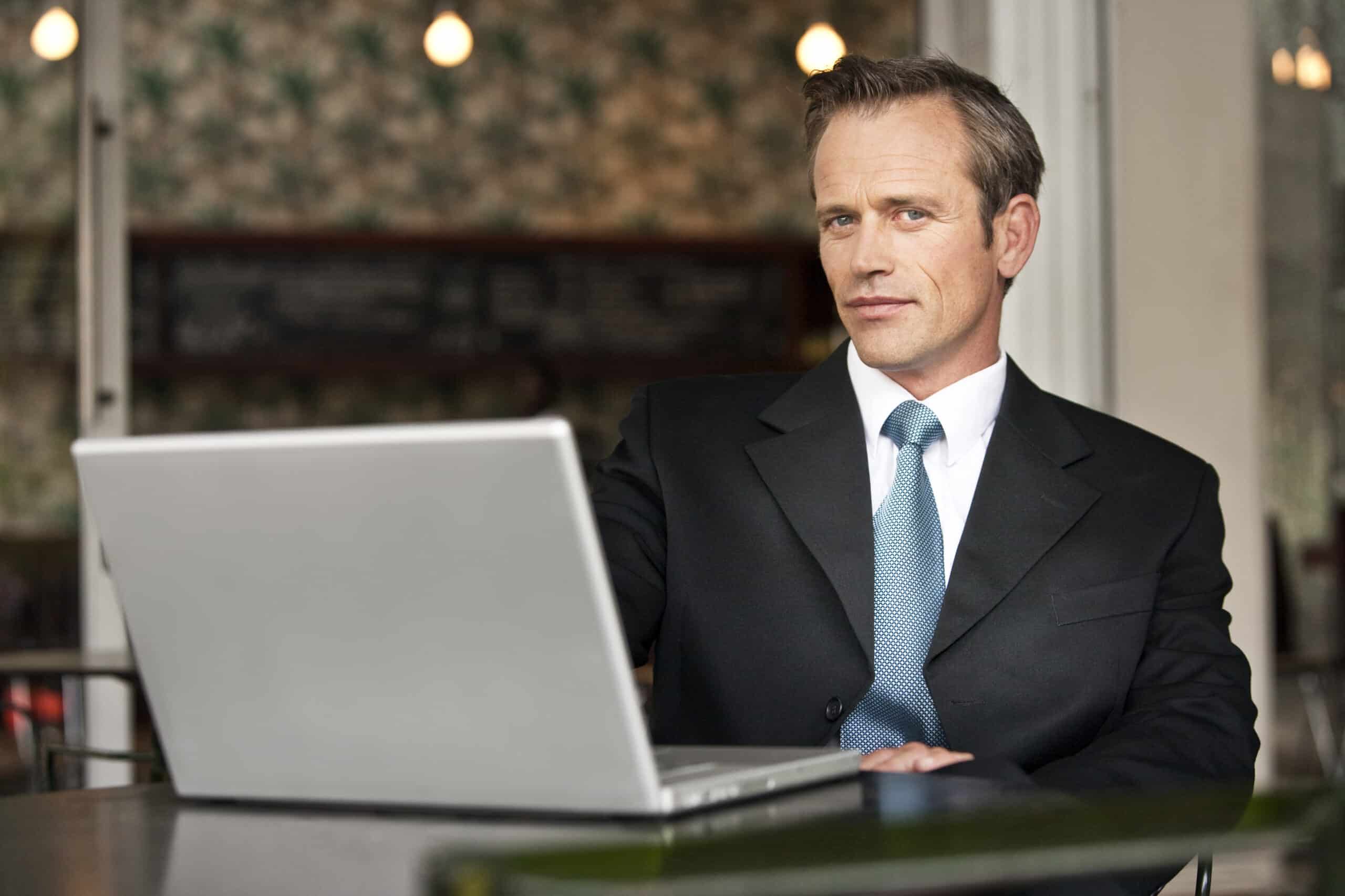 Ein professioneller Mann im Anzug arbeitet an einem Laptop an einem Cafétisch und blickt mit konzentrierter Miene auf den Bildschirm. © Fotografie Tomas Rodriguez