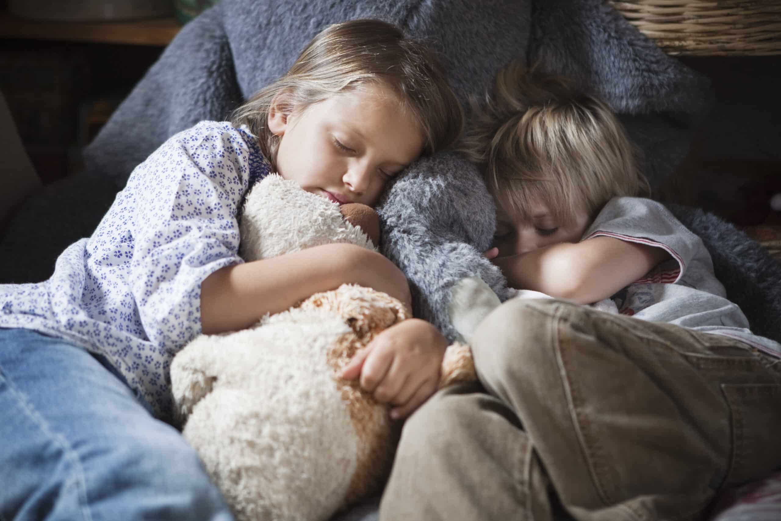 Zwei kleine Kinder schlafen friedlich auf einem großen, gemütlichen Stuhl. Das Mädchen links umarmt ein Stofftier, während der Junge rechts sich an sie gekuschelt hat. Beide haben einen heiteren Gesichtsausdruck und werden von einer Seite von einem sanften Licht beleuchtet. © Fotografie Tomas Rodriguez