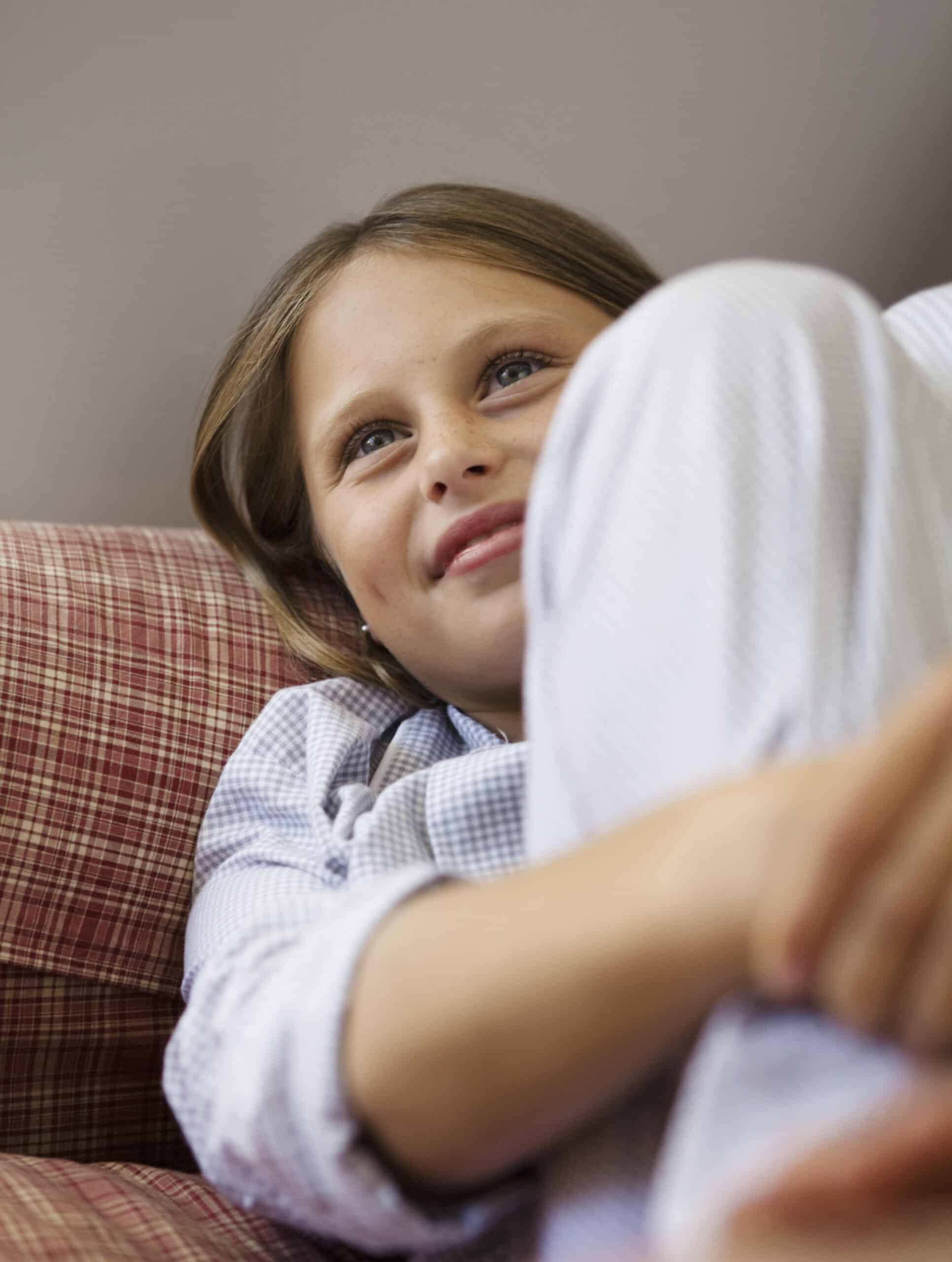 Ein junger Mensch mit hellem Haar und blauen Augen liegt auf einem rotkarierten Sofa und blickt mit nachdenklichem Gesichtsausdruck nach oben. Er trägt ein helles Langarmshirt, die Beine sind angewinkelt, die Arme ruhen auf den Knien. © Fotografie Tomas Rodriguez