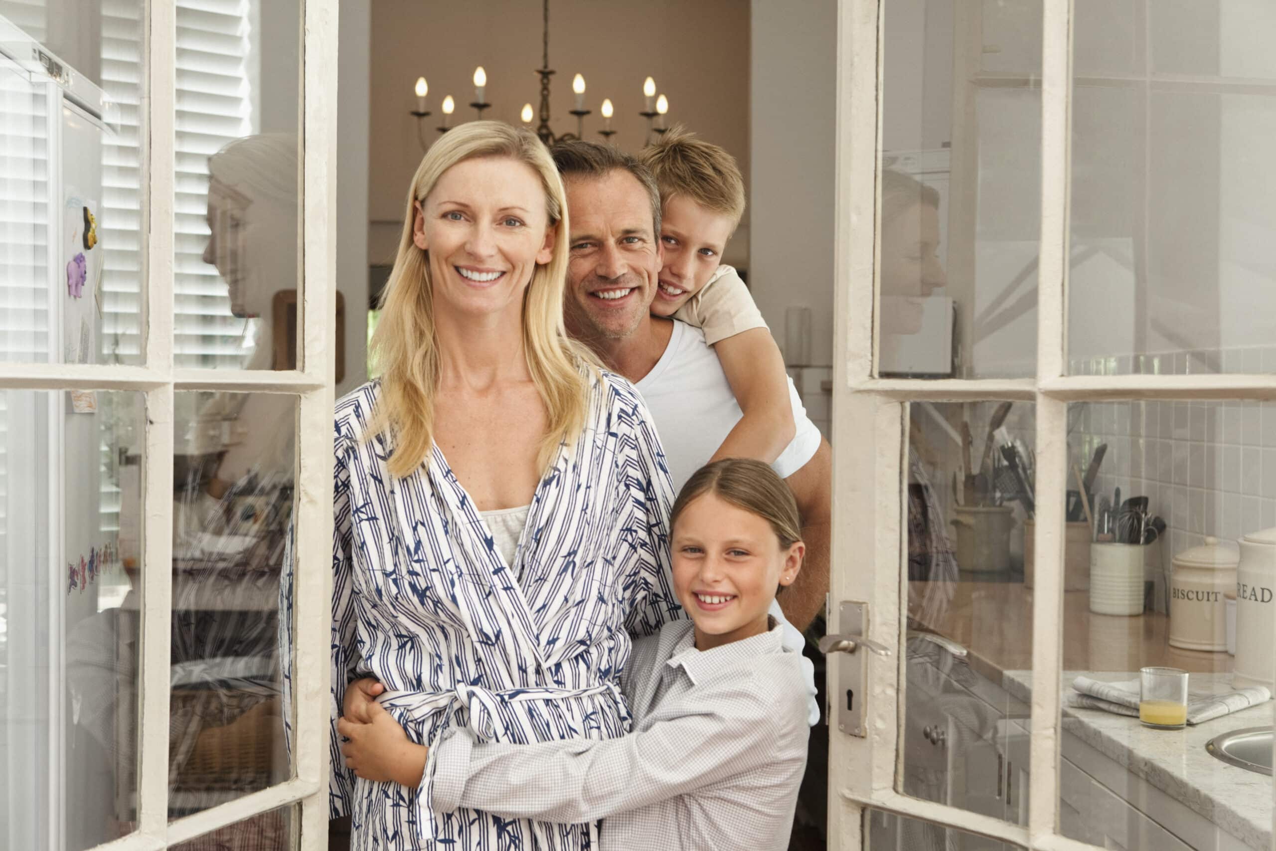 Eine vierköpfige Familie steht zusammen in einer Küche. Eine Frau in einem gemusterten Bademantel steht vorne und lächelt. Hinter ihr lächeln ein Mann und zwei Kinder, ein Junge und ein Mädchen. Die Szene ist gut beleuchtet und im Hintergrund ist ein Kronleuchter zu sehen. © Fotografie Tomas Rodriguez