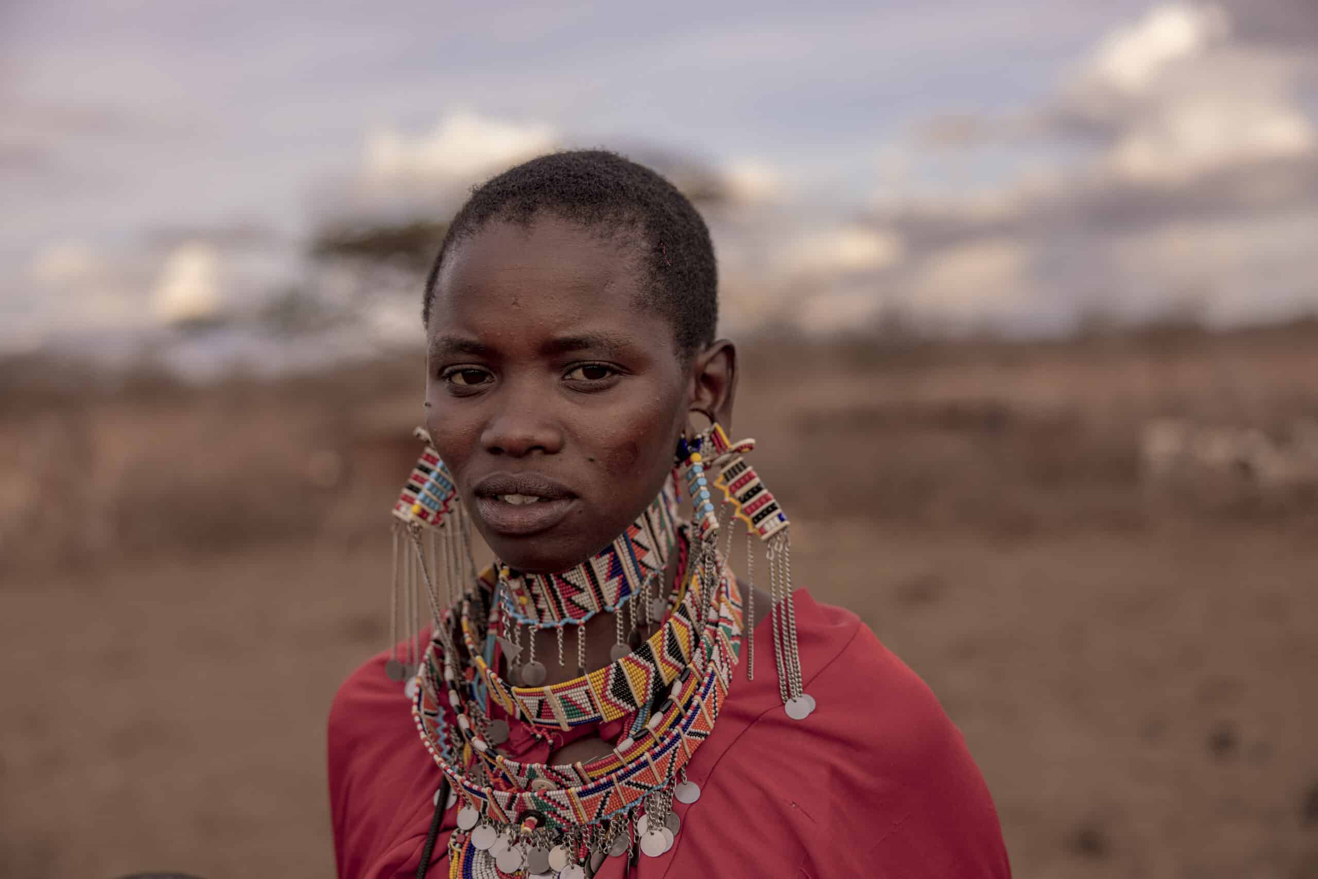 Ein Porträt einer jungen Frau mit traditionellem Perlenschmuck und Ohrringen und heiterem Gesichtsausdruck vor einem unscharfen natürlichen Hintergrund unter einem bewölkten Himmel. © Fotografie Tomas Rodriguez