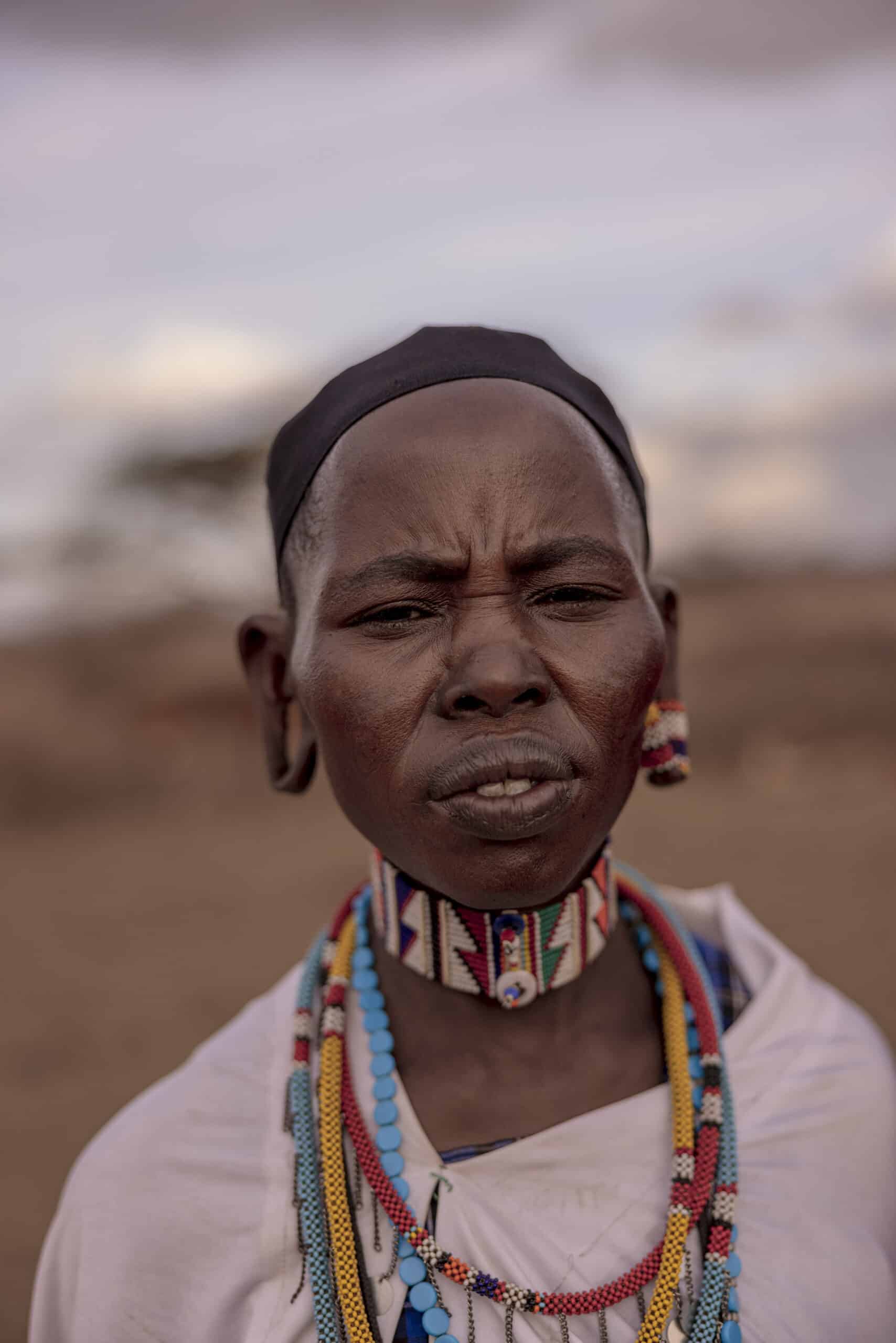Porträt einer Person mit traditionellem Schmuck und Kleidung, einschließlich Halsketten und Stirnband, die vor einem unscharfen natürlichen Hintergrund steht. © Fotografie Tomas Rodriguez