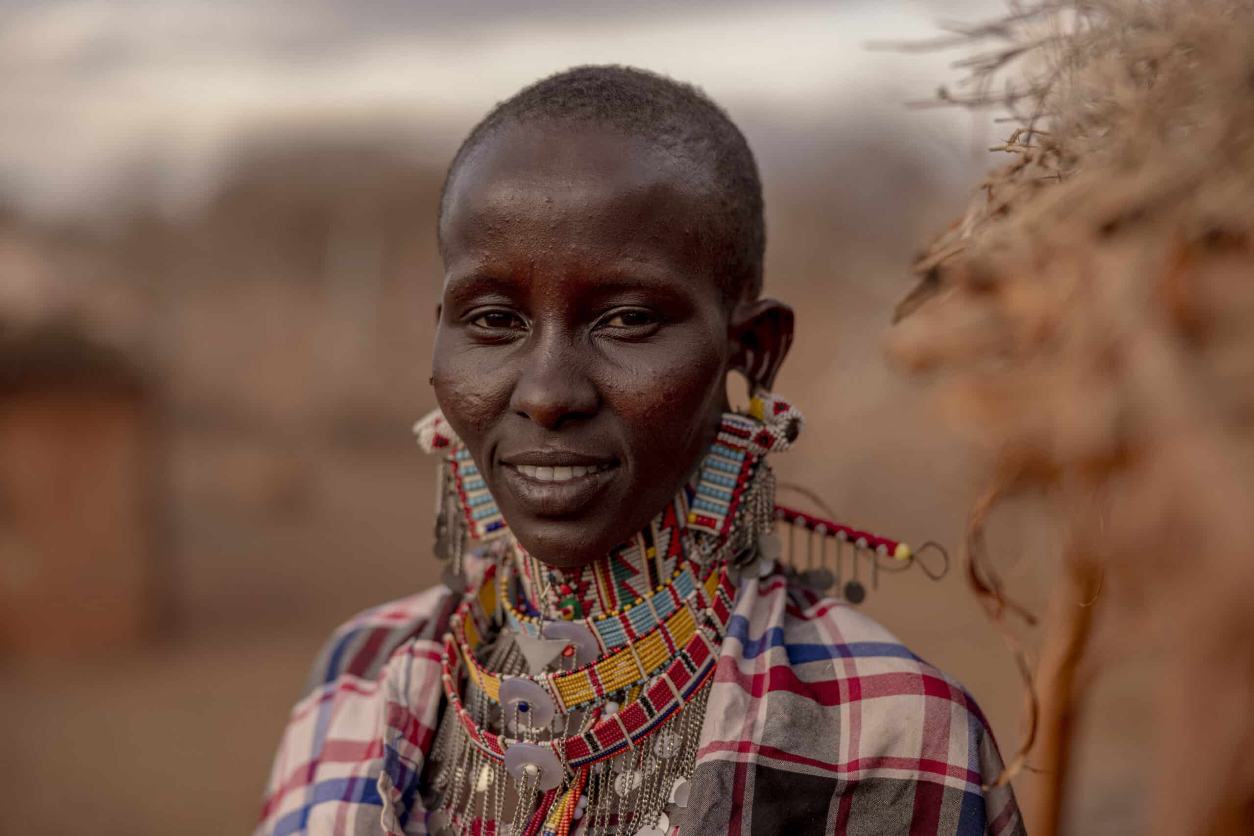 Das Porträt einer Frau mit traditionellen Perlenketten und Ohrringen, die ein kariertes Hemd trägt und sanft lächelt, vor einem unscharfen Hintergrund, der eine natürliche Umgebung einfängt. © Fotografie Tomas Rodriguez