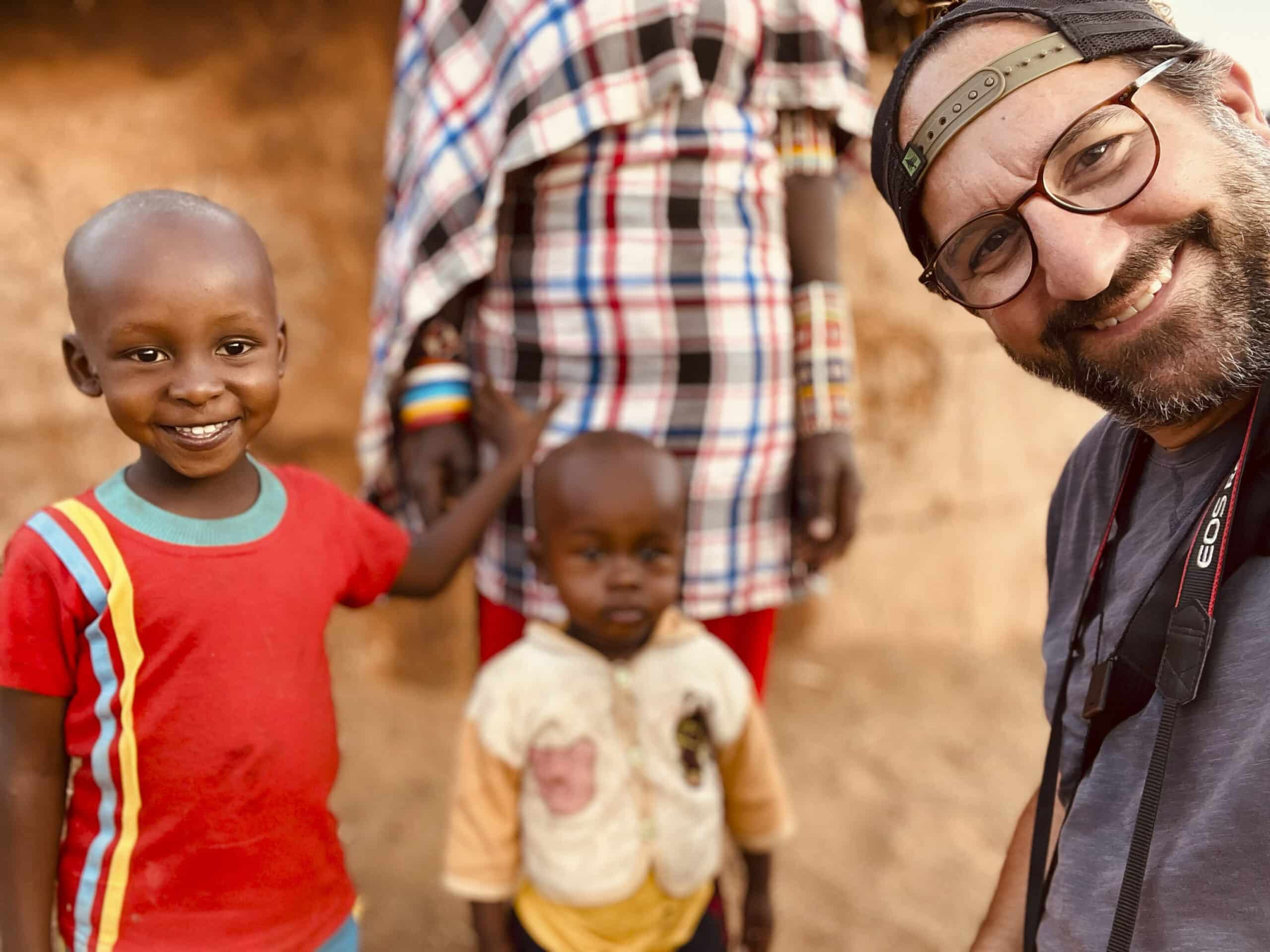 Ein Mann mit Brille und Baseballkappe lächelt in die Kamera. Neben ihm stehen zwei kleine Kinder auf einer sandigen Fläche. Im Hintergrund ist der Teil einer anderen Person zu sehen. © Fotografie Tomas Rodriguez