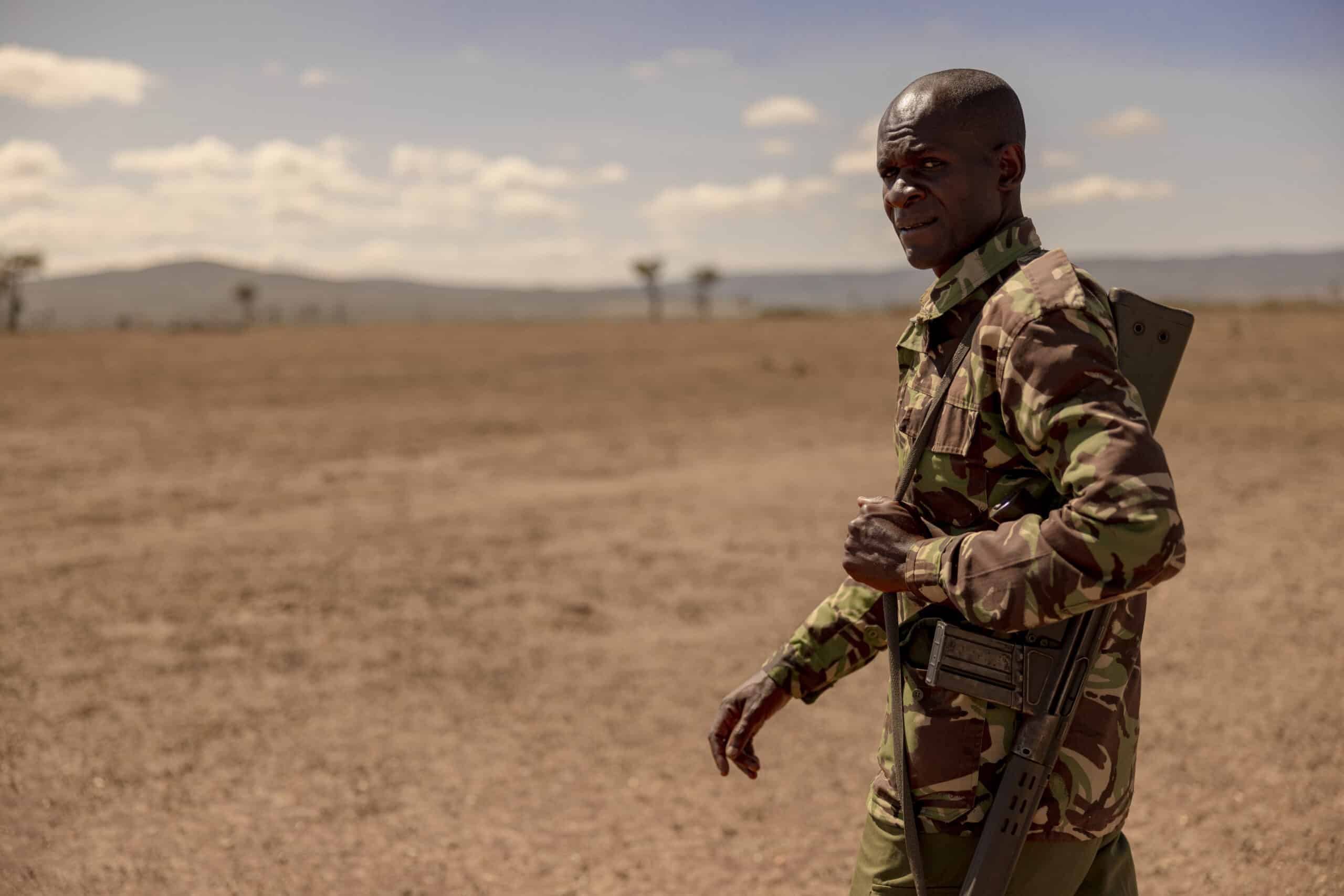 Ein Soldat in Tarnuniform steht in einer kargen Wüstenlandschaft und blickt mit ernster Miene zurück. Er trägt einen Rucksack und über ihm ist der Himmel klar. © Fotografie Tomas Rodriguez