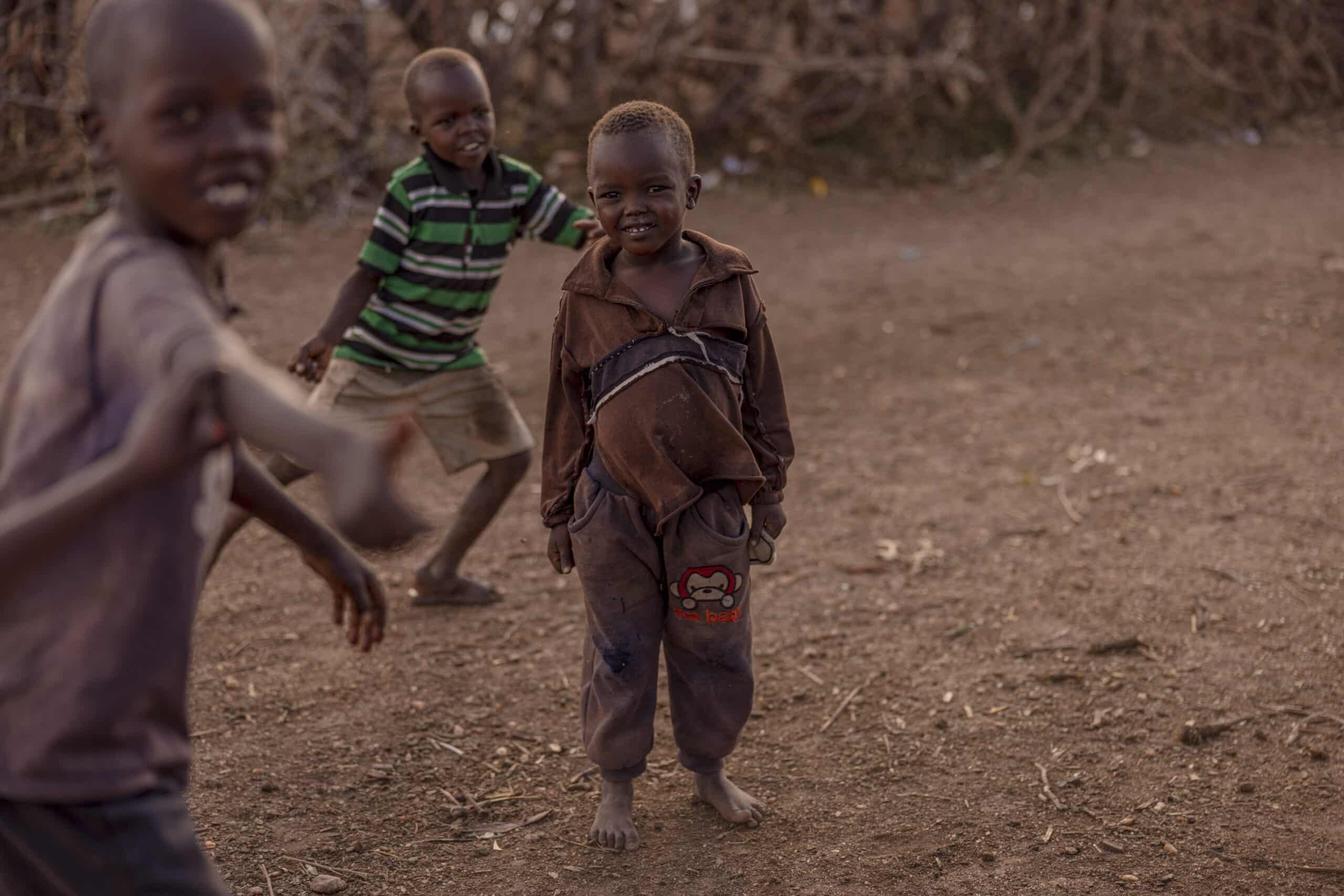 Drei kleine Kinder spielen in einer ländlichen Gegend. Ein Kind lächelt breit und rennt in Richtung Kamera, während die anderen im Hintergrund fröhlich dreinschauen. © Fotografie Tomas Rodriguez