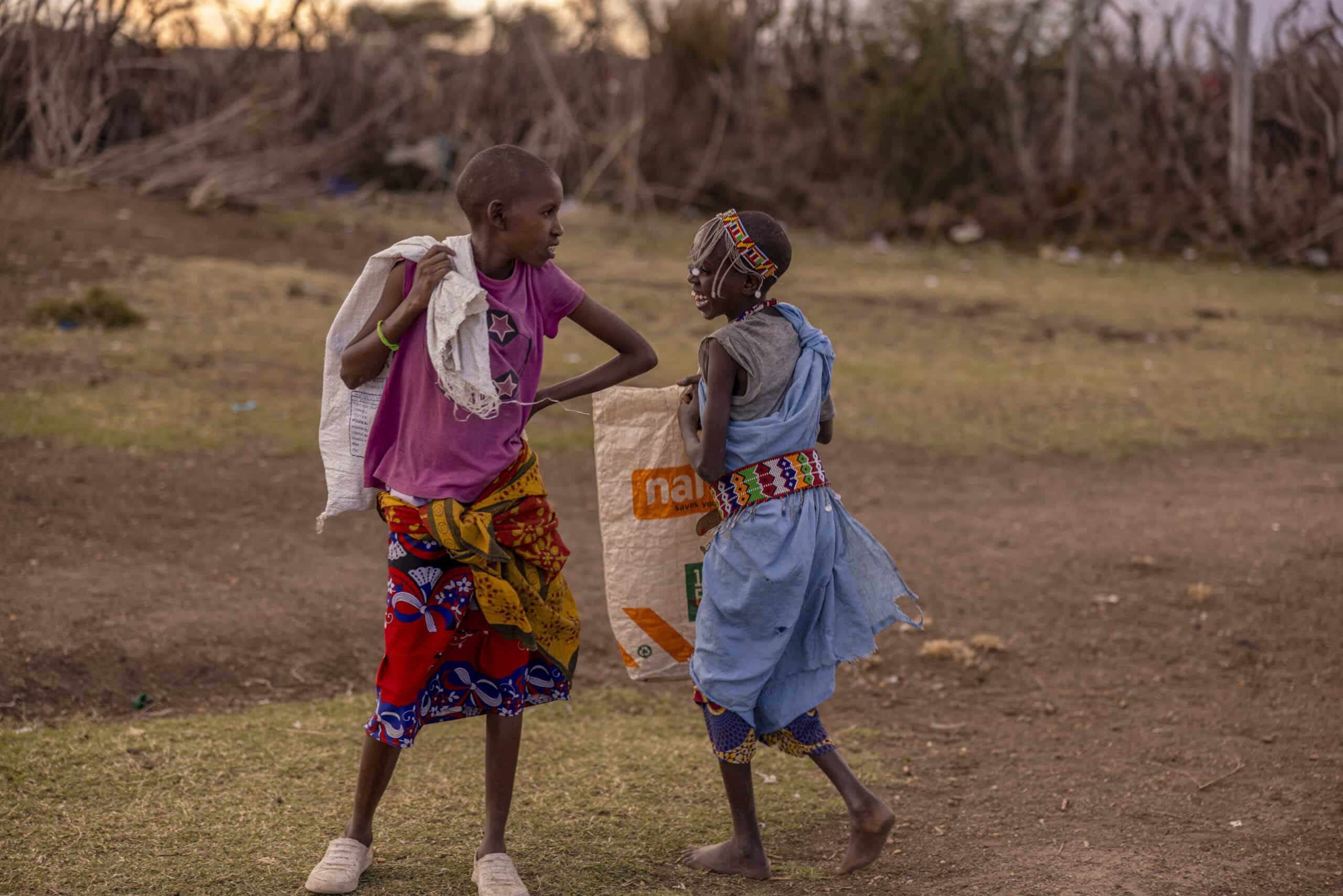 Zwei Kinder in traditioneller afrikanischer Kleidung tanzen in der Abenddämmerung im Freien verspielt, im Hintergrund eine Naturlandschaft. © Fotografie Tomas Rodriguez