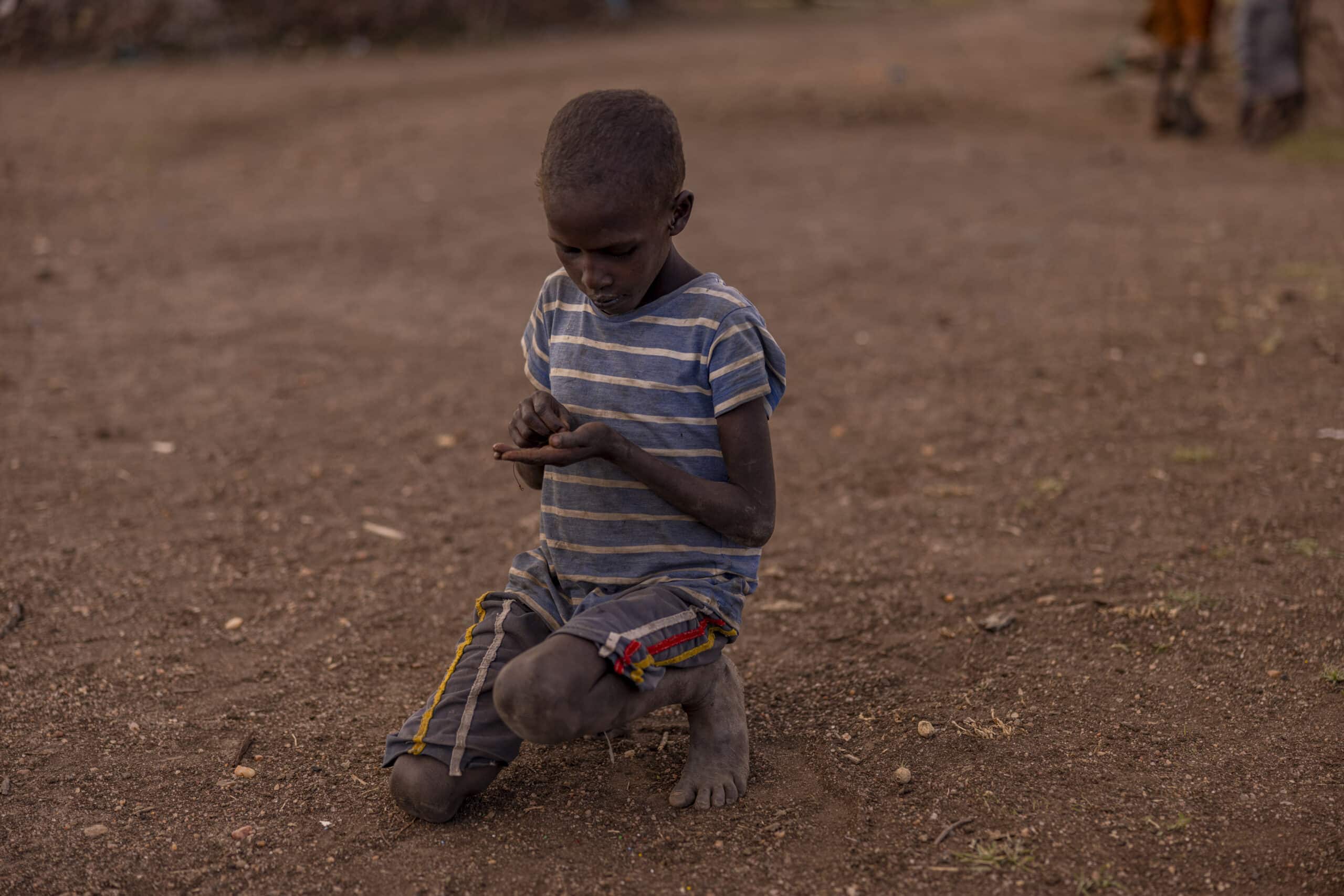 Ein kleiner Junge in gestreiftem Hemd und Shorts kniet auf einem staubigen Boden und konzentriert sich auf ein Smartphone, das er in seinen Händen hält. © Fotografie Tomas Rodriguez