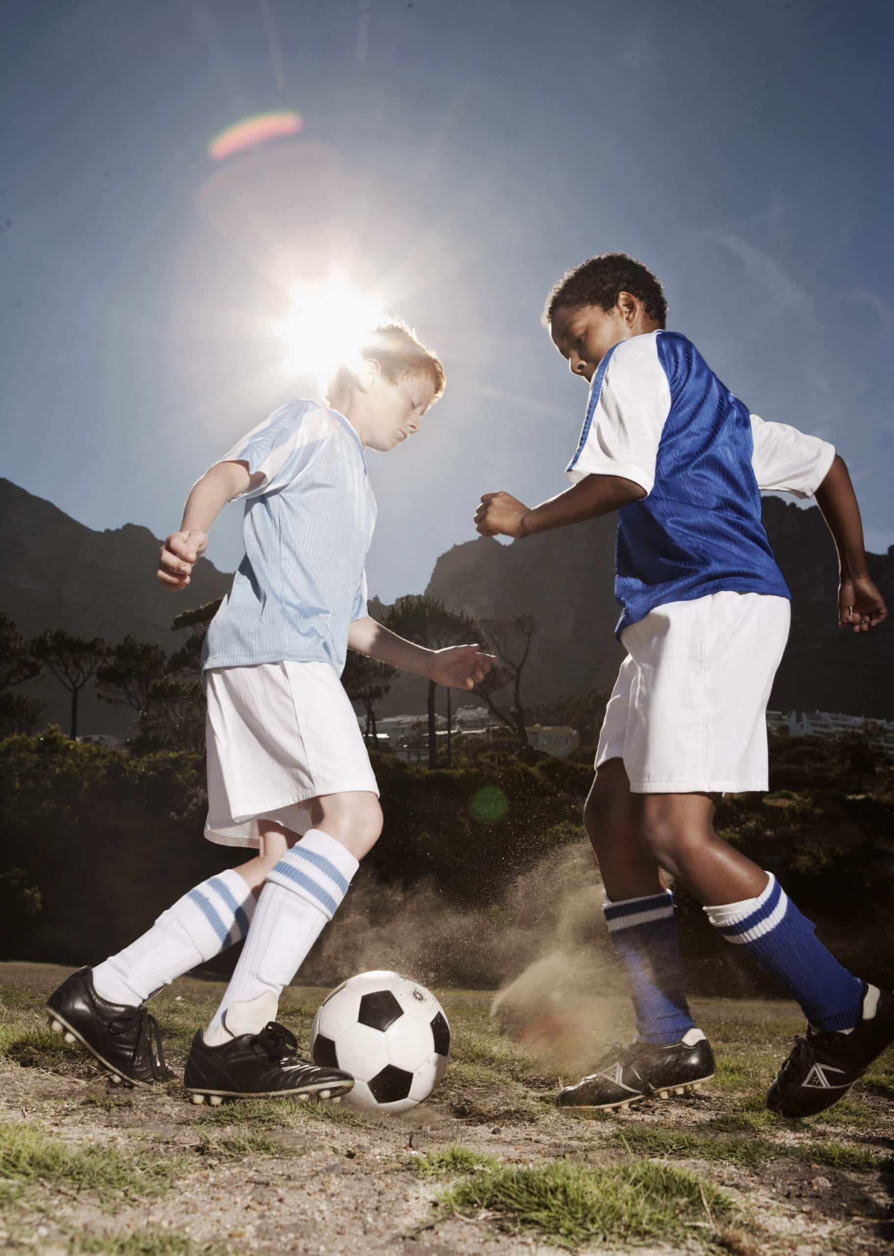 Zwei junge Fußballspieler sind in ein Spiel verwickelt. Einer trägt ein hellblaues Trikot und weiße Shorts, der andere ein blaues Trikot und weiße Shorts. Beide konzentrieren sich auf einen Fußball auf dem Boden. Hinter ihnen scheint hell die Sonne. © Fotografie Tomas Rodriguez