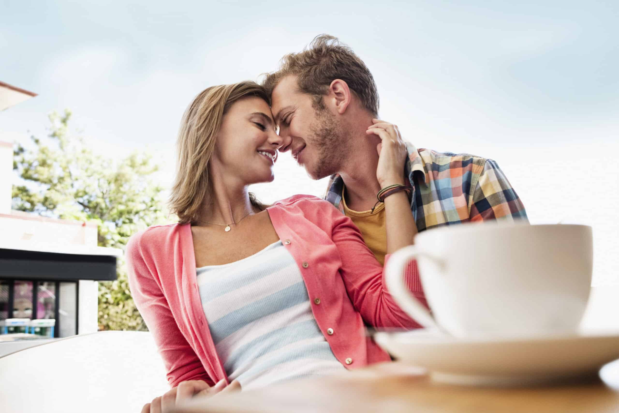 Ein junges Paar, das an einem Cafétisch sitzt und sich liebevoll die Stirn berührt. Im Vordergrund ist eine Kaffeetasse zu sehen, die einen Moment der Zuneigung und Intimität vermittelt. © Fotografie Tomas Rodriguez