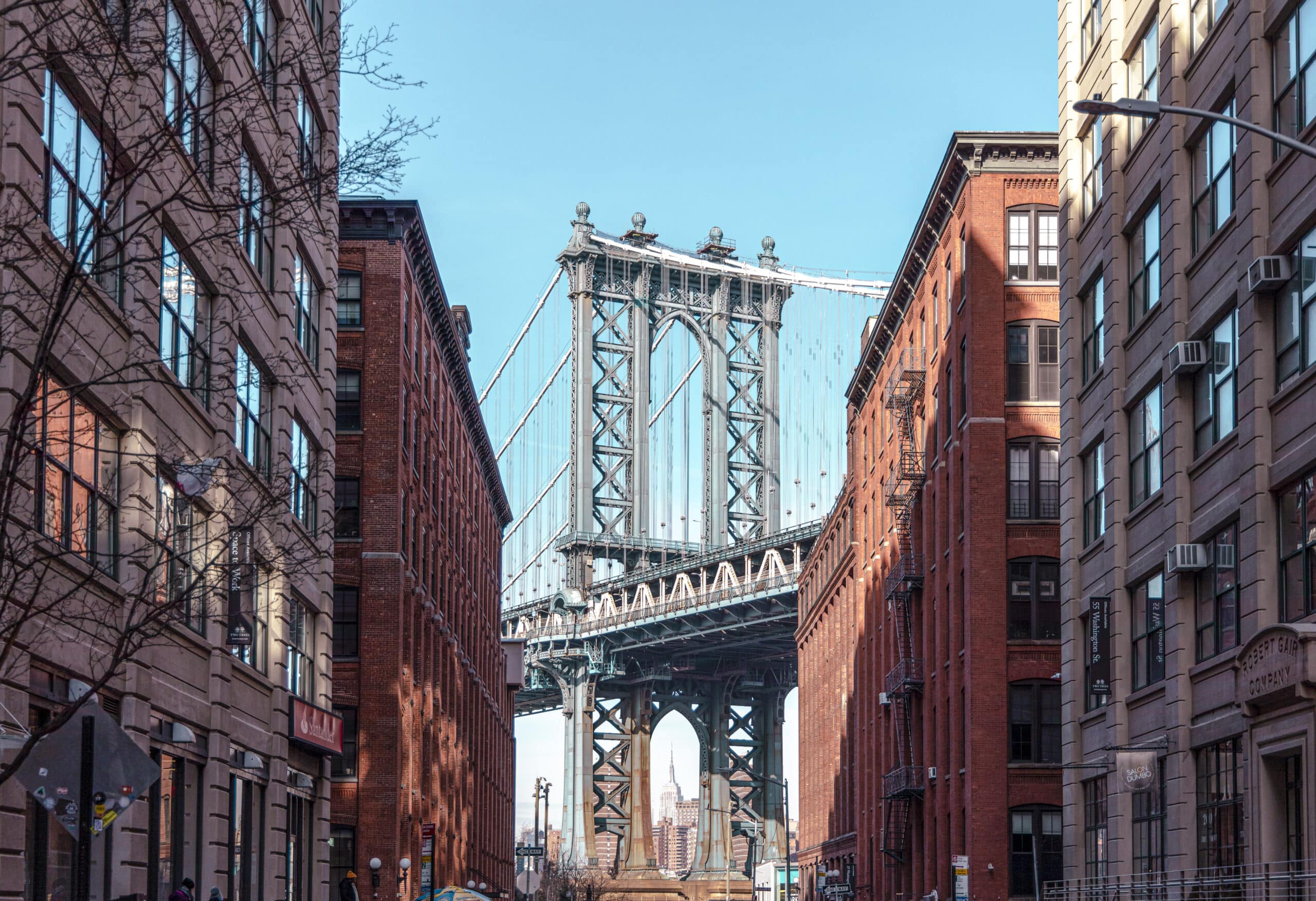 Blick auf die Manhattan Bridge von Dumbo, Brooklyn, eingerahmt von Backsteingebäuden unter einem klaren blauen Himmel. © Fotografie Tomas Rodriguez