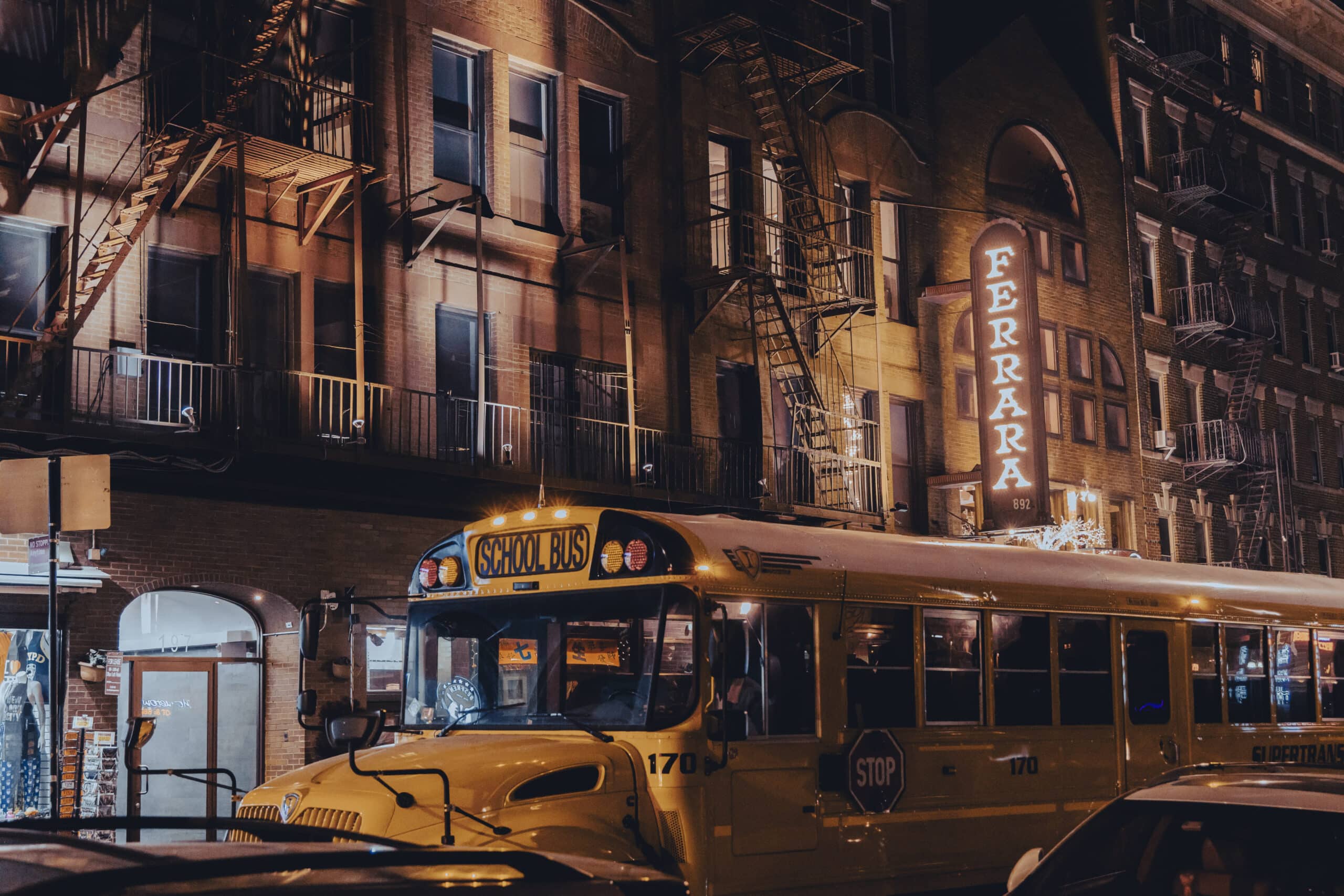 Ein gelber Schulbus parkt nachts auf einer Stadtstraße. Im Hintergrund sind beleuchtete Schilder und Gebäude zu sehen, die eine geschäftige Stadtatmosphäre schaffen. © Fotografie Tomas Rodriguez
