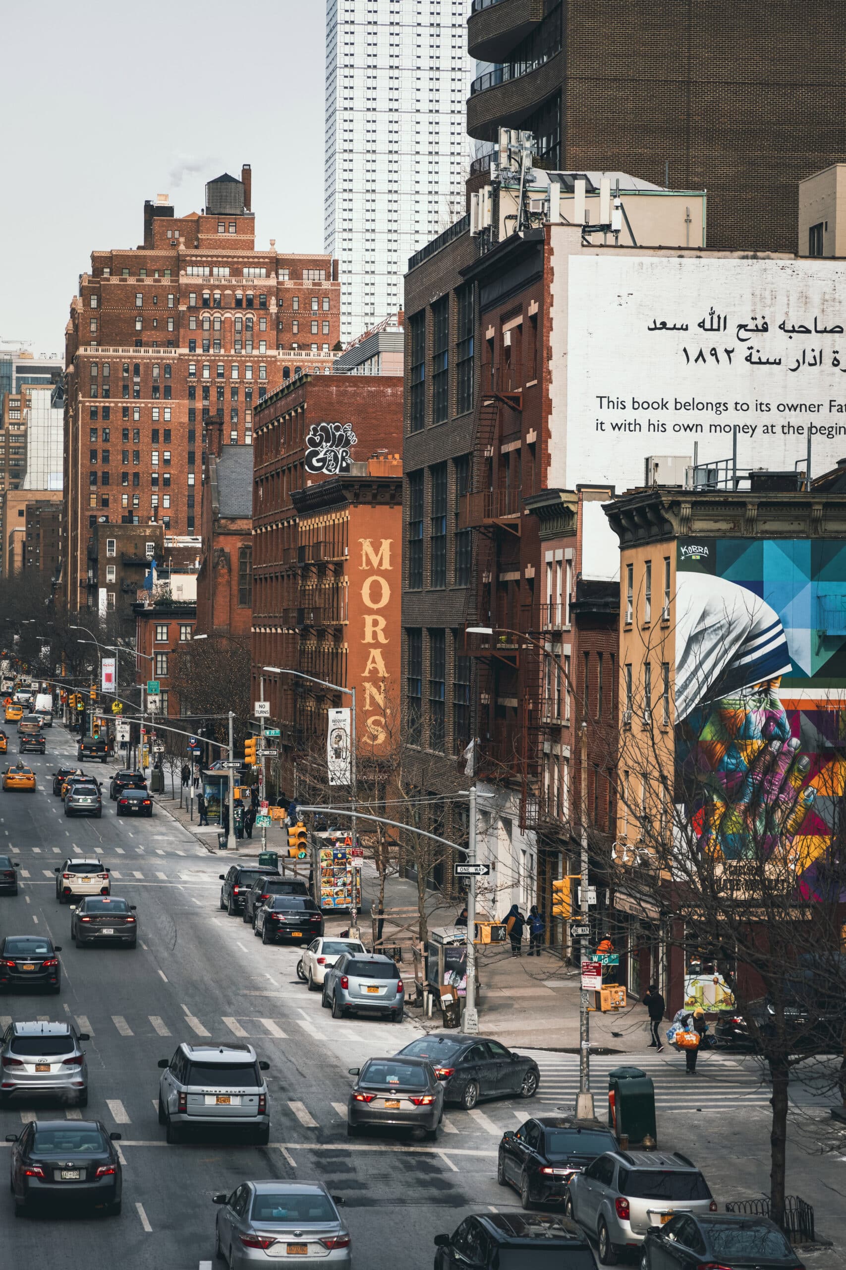 Städtische Straßenszene mit Autos und älteren Backsteingebäuden, darunter eines mit einem Schild für „Moran’s“, im Kontrast zu einem eleganten modernen Wolkenkratzer im Hintergrund. © Fotografie Tomas Rodriguez