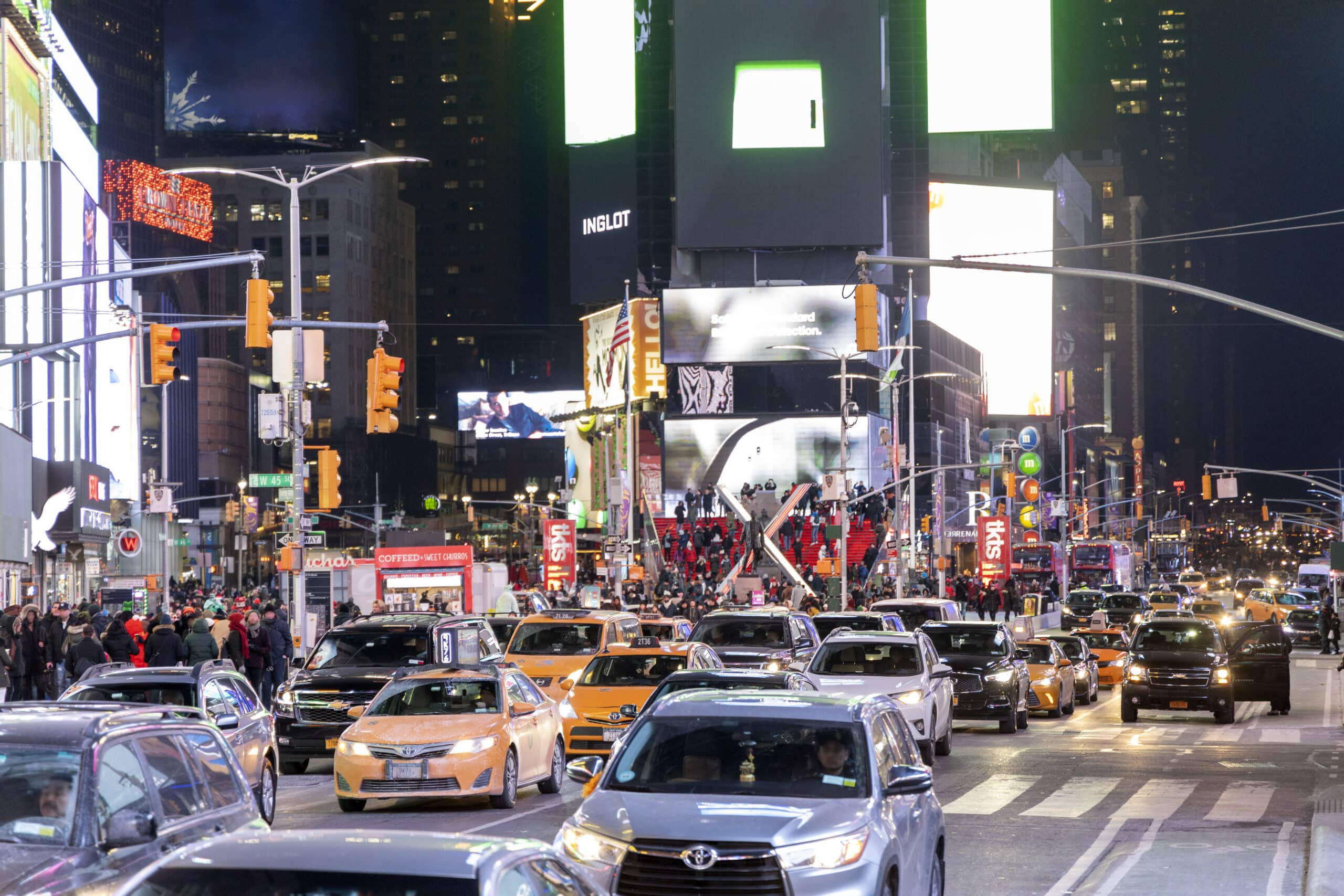 Eine belebte Stadtstraße bei Nacht, beleuchtet von Neonlichtern und Werbetafeln, voller Autos und Fußgänger. Die Szene fängt eine lebendige urbane Atmosphäre ein, wie sie typisch für ein geschäftiges Innenstadtgebiet ist. © Fotografie Tomas Rodriguez
